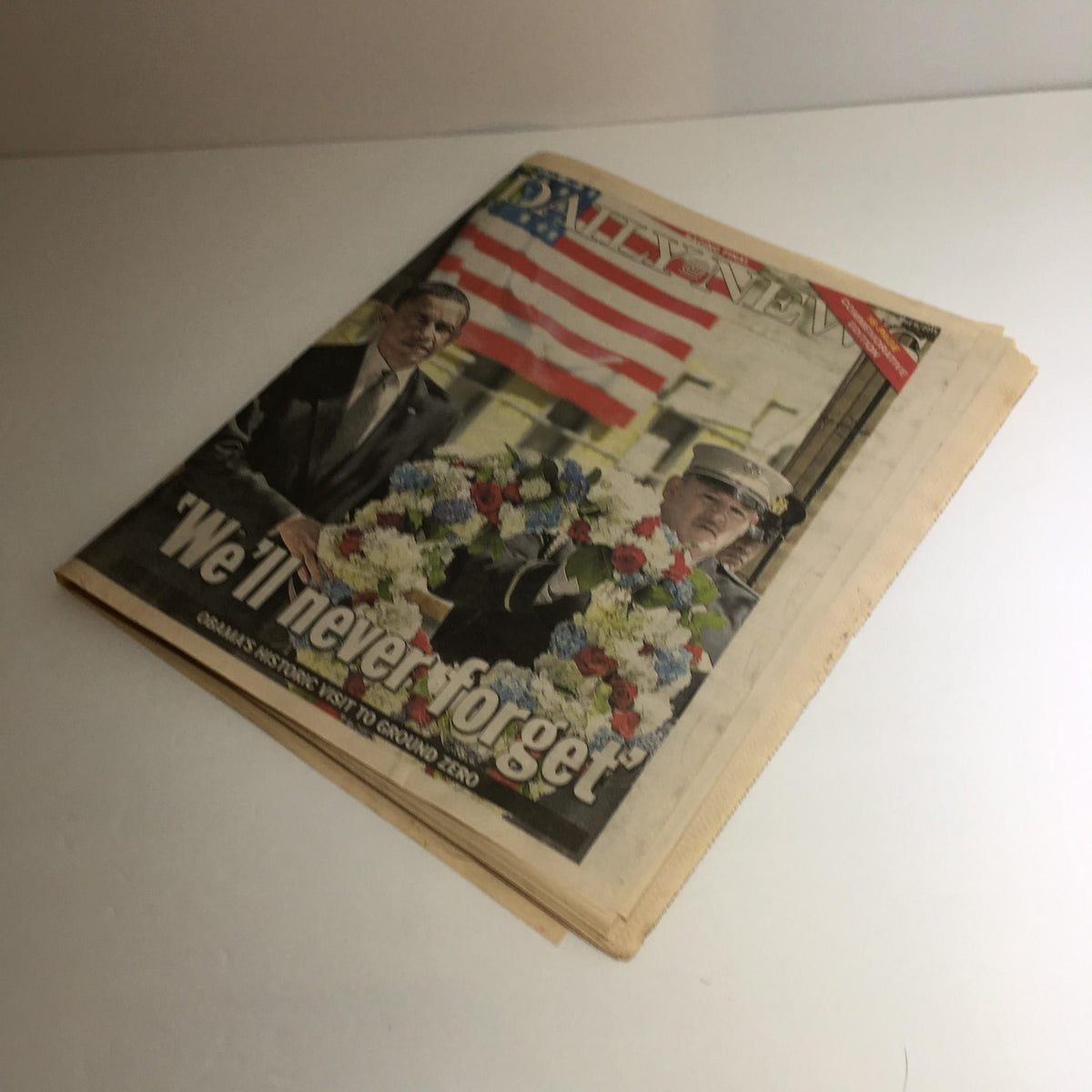 NY Daily News front page from May 6, 2011, featuring President Obama presenting flowers at Ground Zero, highlighted with the words 'We'll Never Forget' to commemorate the event.