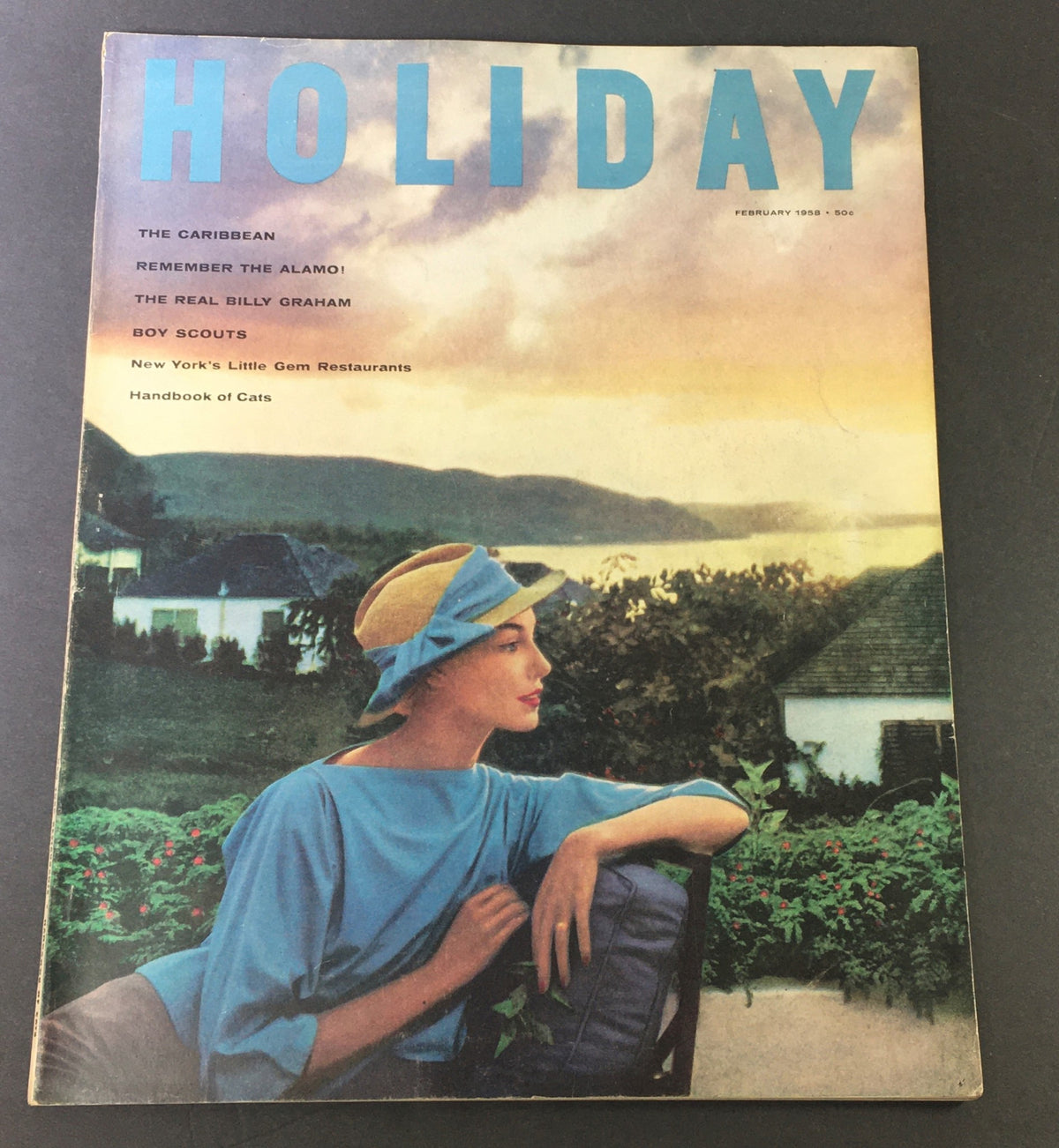 Cover of VTG Holiday Magazine February 1958 showcasing The Caribbean and The Real Billy Graham with a vintage illustration of a woman in a blue outfit and sun hat beside lush greenery.