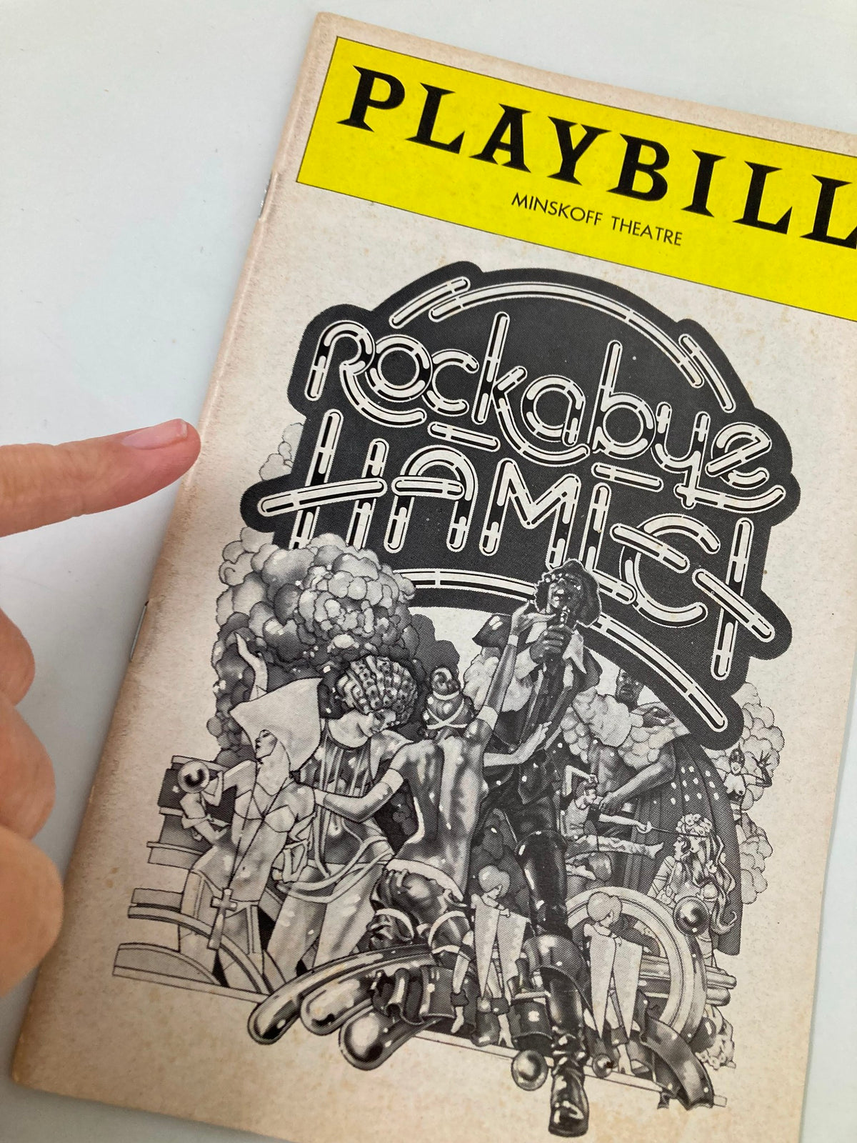 1976 Playbill for Rockabye Hamlet at Minskoff Theatre, showcasing the intricate artwork and a finger pointing to the cover.