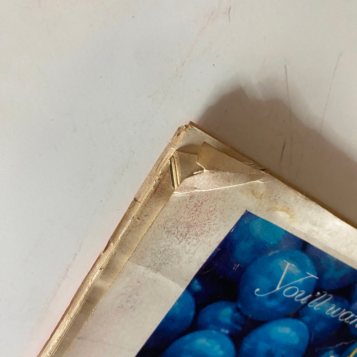 Close-up of the corner of the back cover of Vintage Time Magazine May 7, 1956 showing wear and tear and a seal with printed text.