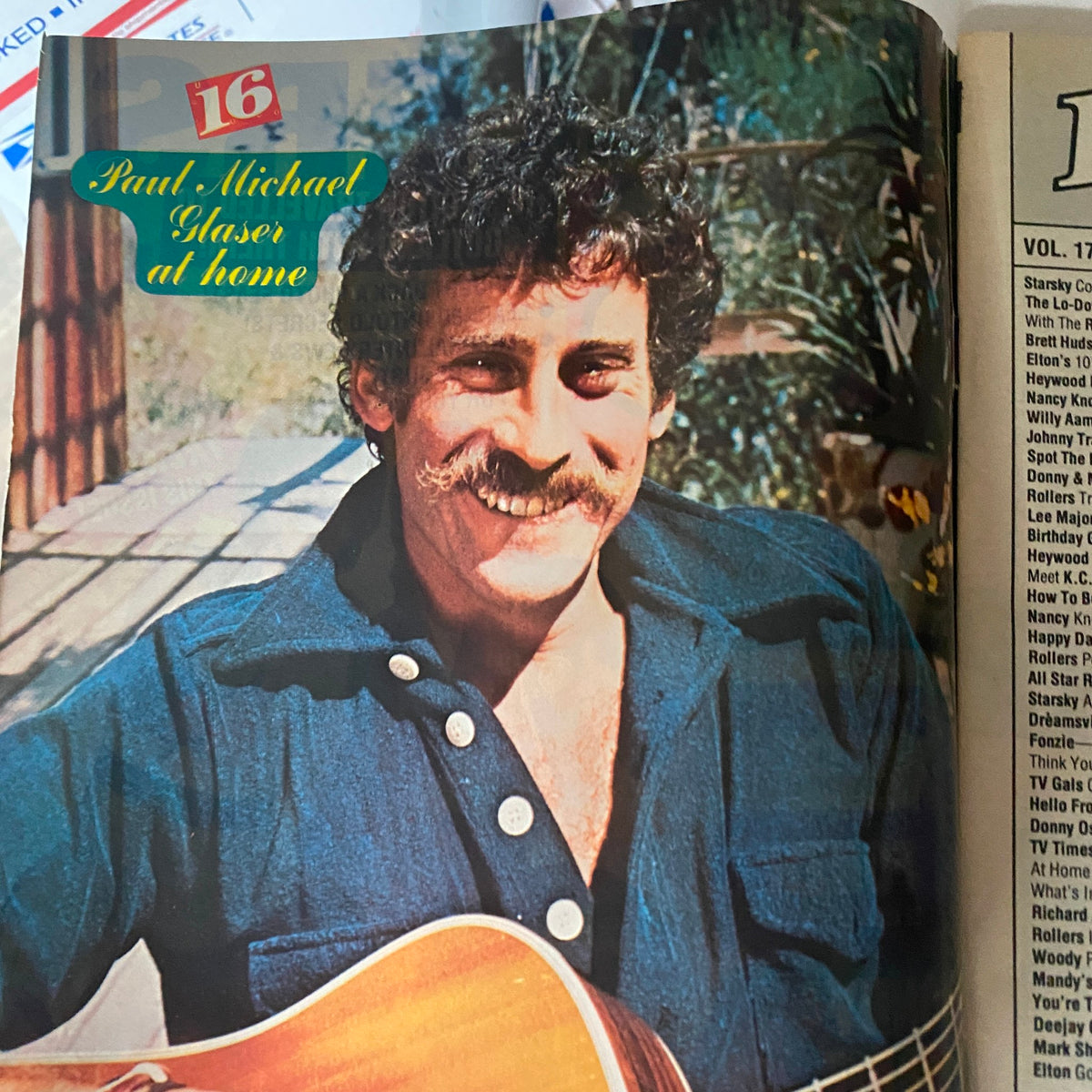 Photograph of Paul Michael Glaser featured in June 1976 16 Magazine, capturing the actor at home with a guitar.