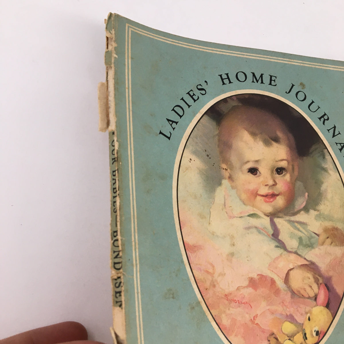 Close-up view of the cover of Ladies' Home Journal 'Our Babies Their Feeding, Care and Training' by Dr. Herman, showing soft colors and the portrait of an infant.