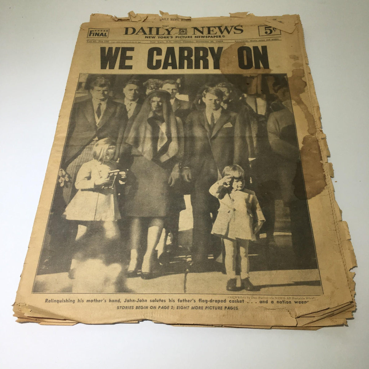 Vintage NY Daily News edition from November 26, 1963 titled 'We Carry On,' featuring a somber image related to JFK's funeral procession, depicting family members and friends.