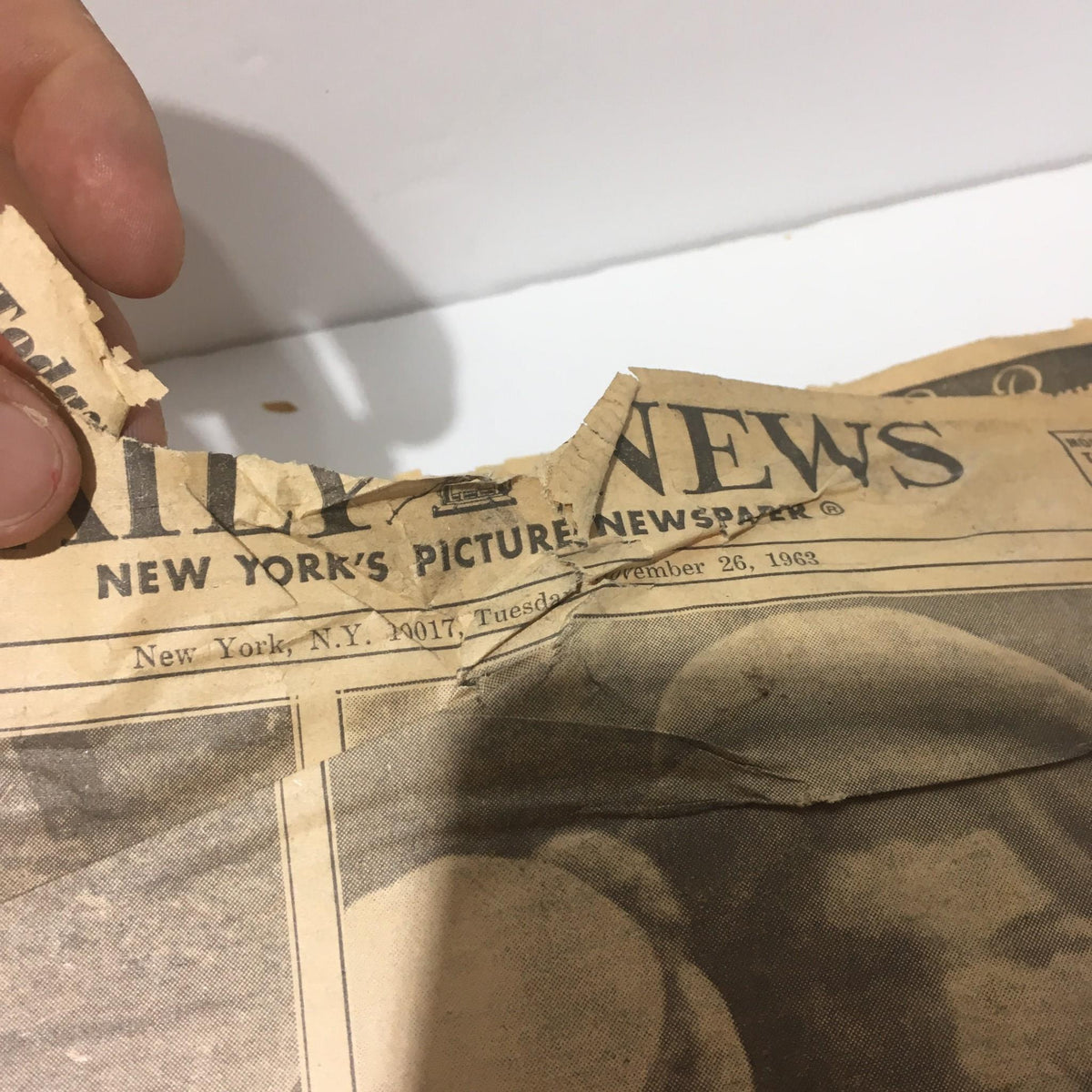 Torn edge of a vintage New York Daily News from November 26, 1963, titled 'We Carry On', showing partial newspaper title with visible wear.