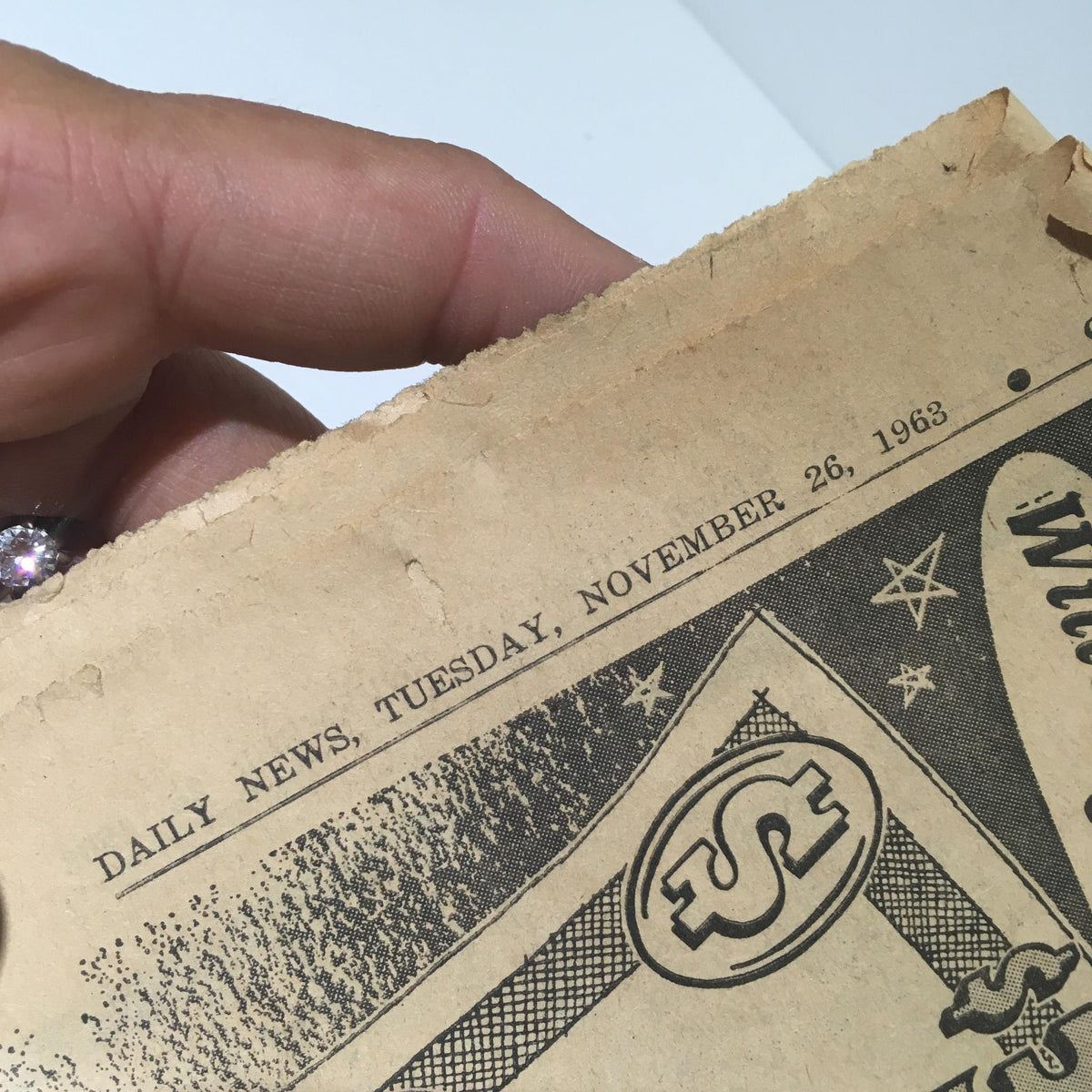 Detail shot of the date on the top corner of a vintage New York Daily News from November 26, 1963, titled 'We Carry On', showing the newspaper's age.