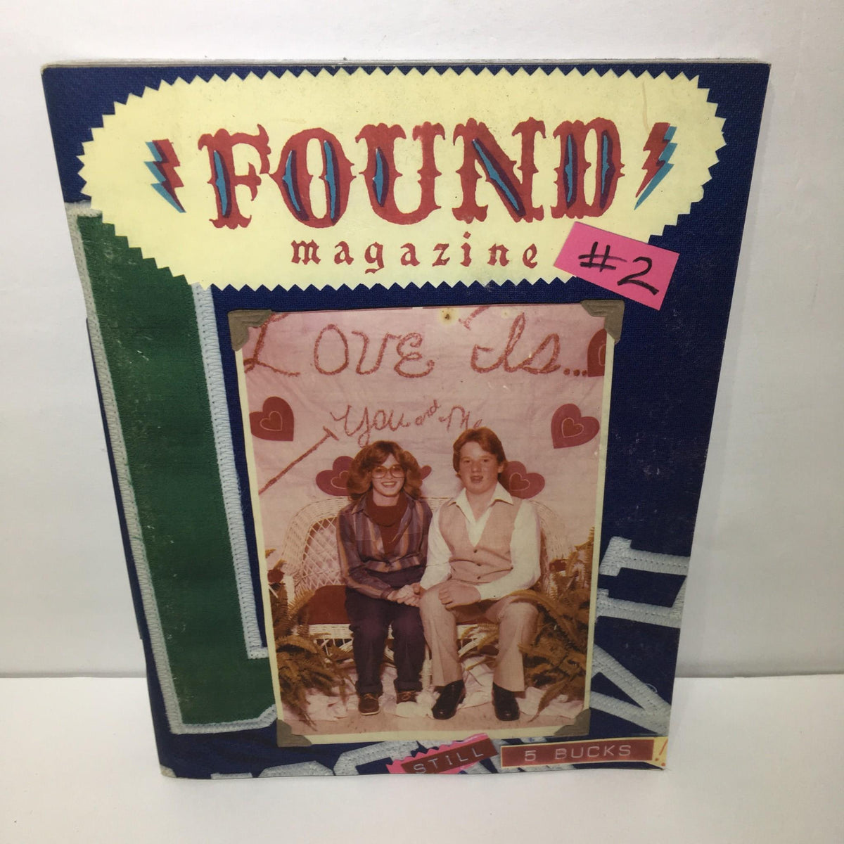 Cover of Found Magazine #2 featuring a vintage photograph of two people on a decorative background with a handwritten message and hearts.