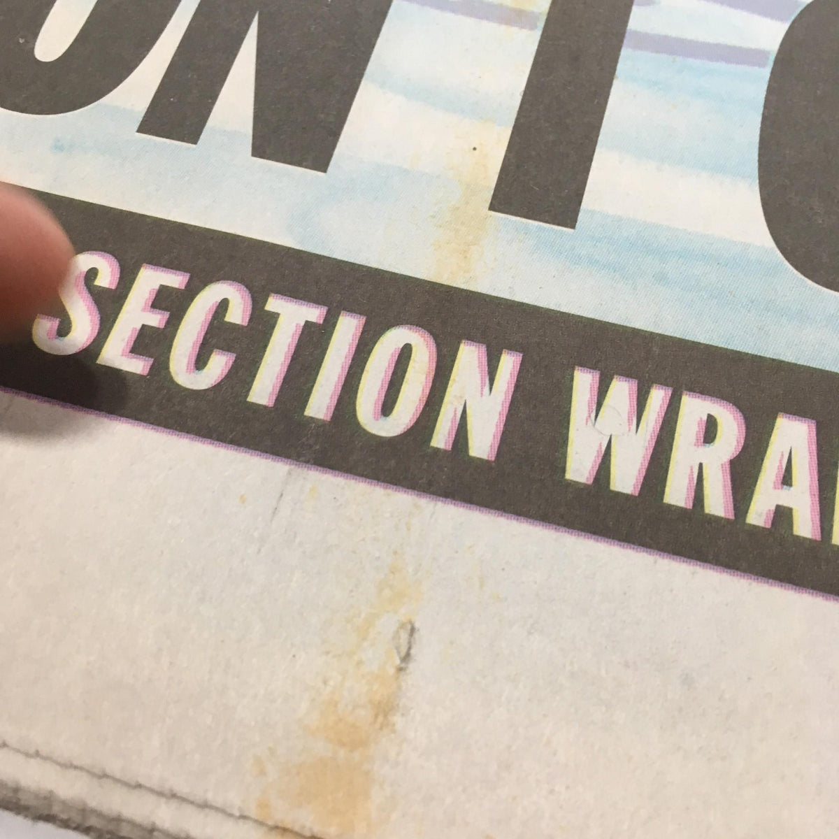 Close-up of the NY Daily News text 'SECTION WRAPS' located at the bottom of the front page, highlighting a stain.