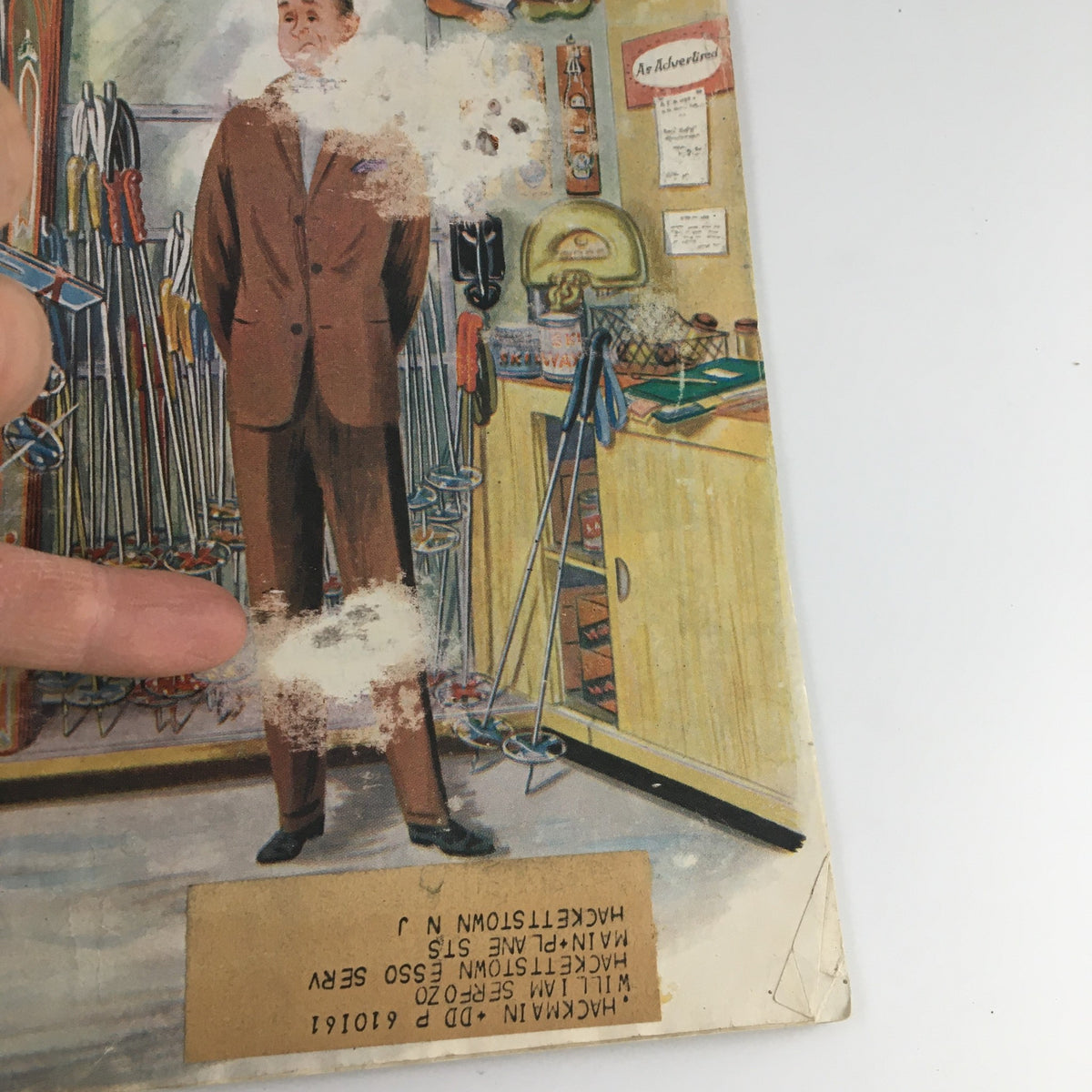 Detail of the illustration from The Saturday Evening Post March 4 1961, depicting a man in a brown suit surrounded by skiing gear, with a label on the bottom.