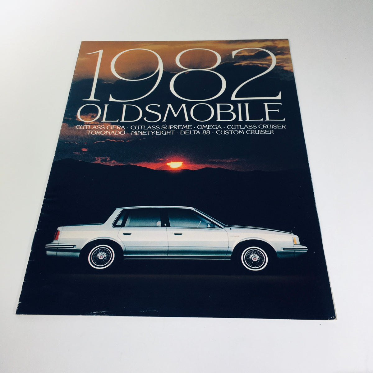 1982 Oldsmobile Cutlass Ciera, Supreme, Omega, Cruiser brochure featuring a silver Oldsmobile vehicle against a sunset backdrop.