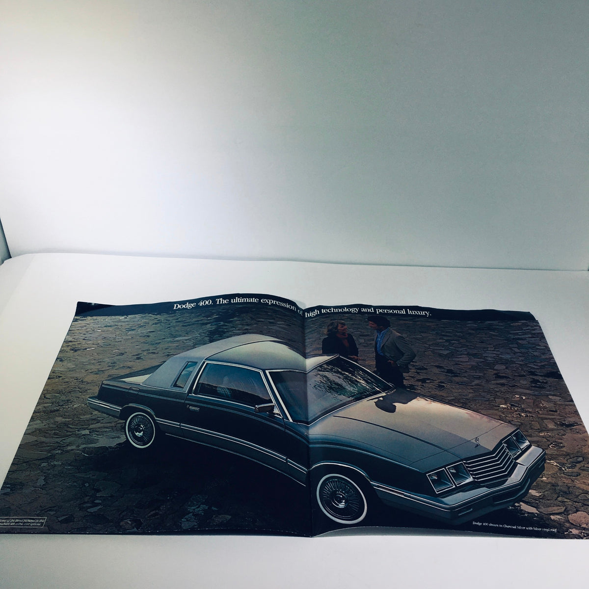 Open view of the 1982 Dodge 400 car sale brochure showcasing the vehicle in Charcoal Silver alongside two individuals discussing its features.