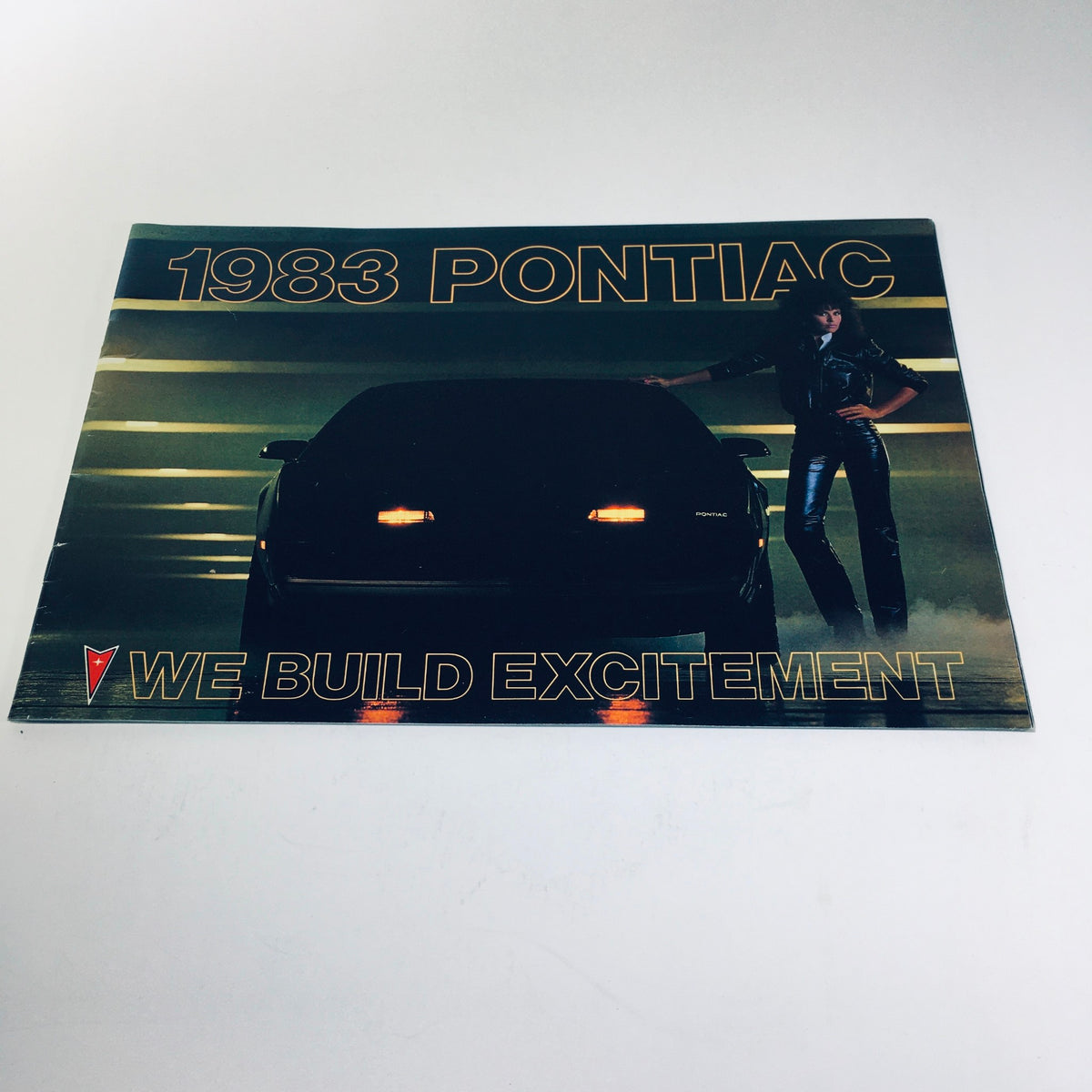 1983 Pontiac 6000 brochure showcasing a sleek car with the tagline 'We Build Excitement', featuring a model in stylish attire against a dramatic backdrop, highlighting the vintage automotive design and advertising style of the early 1980s.