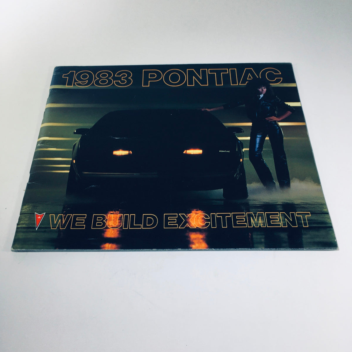 1983 Pontiac 2000 5.8 Liter V-8 Engine Grand Prix Car Sale Brochure showcasing a sleek black car in a dynamic pose, emphasizing the tagline 'We Build Excitement'.