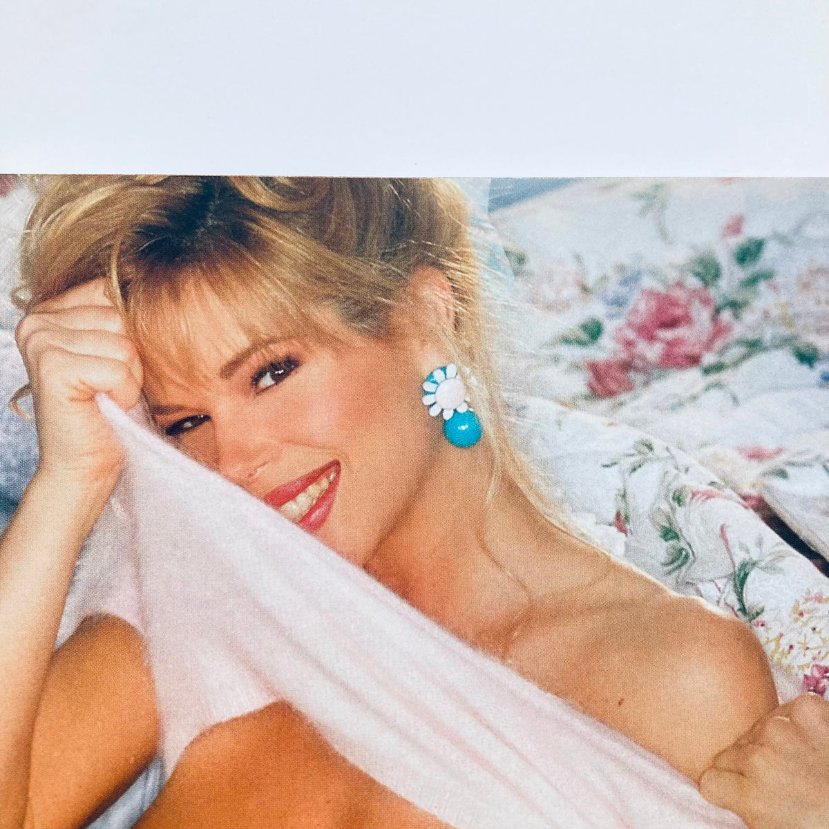 Playboy's Playmates Exposed Magazine 1998 Covergirl Shannon Leahy smiling and playfully holding a pink garment, featuring vibrant blue earrings, against a floral backdrop.