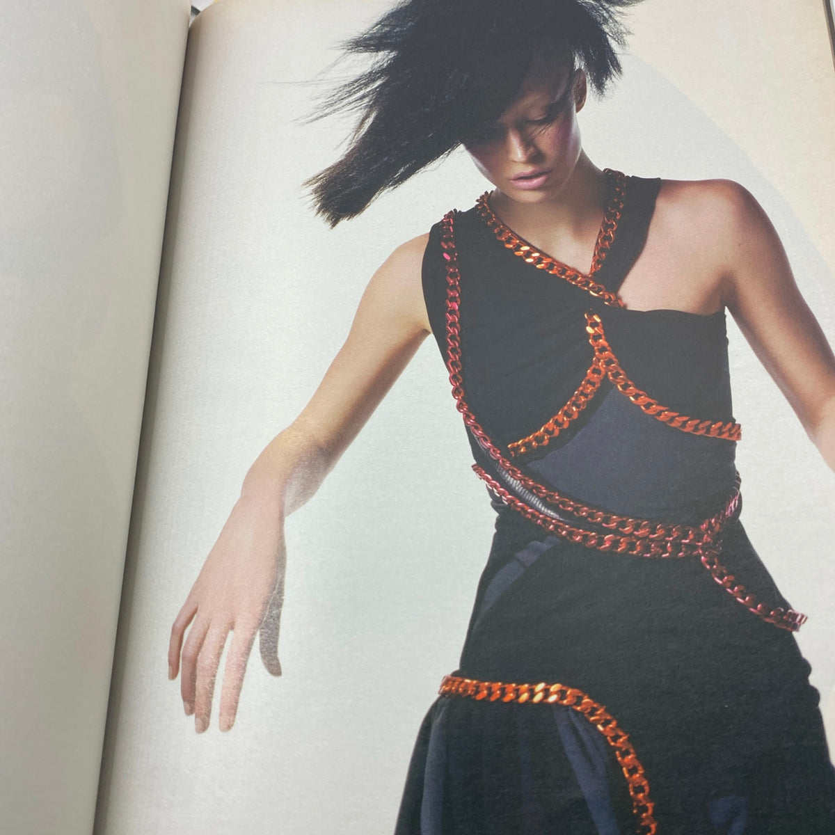 High-fashion editorial image from W Magazine July 2004, featuring a model in a stylish black dress with distinctive chain detailing, showcasing contemporary fashion trends.