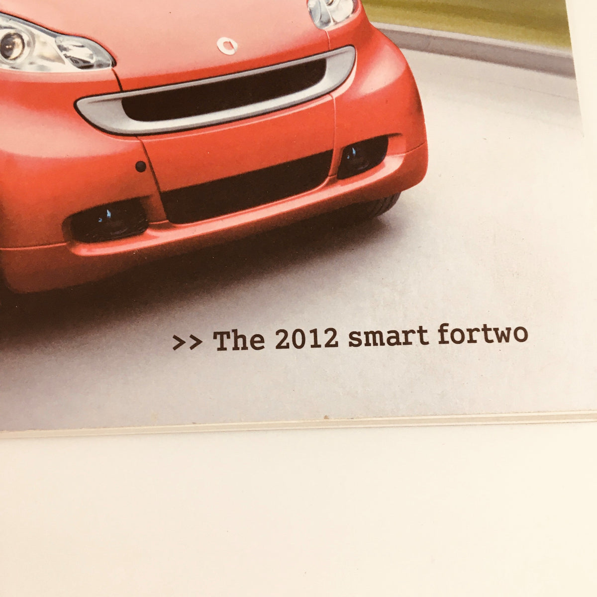 Close-up view of the front of the red 2012 Smart Fortwo City Solution Hill-Start Assist Car Brochure, highlighting the car's design and the text 'The 2012 smart fortwo'.