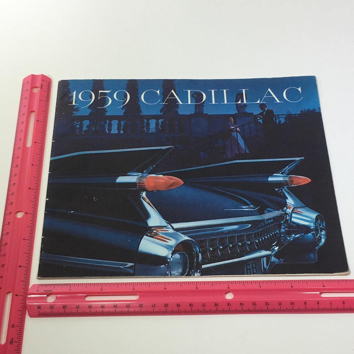 1959 Cadillac Fleetwood Sixty Special Sedan V-Type Engine Car Sale Brochure cover featuring a stylish classic Cadillac, showcasing its distinctive tail fins and chrome details, with a glamorous backdrop, and a ruler for scale.