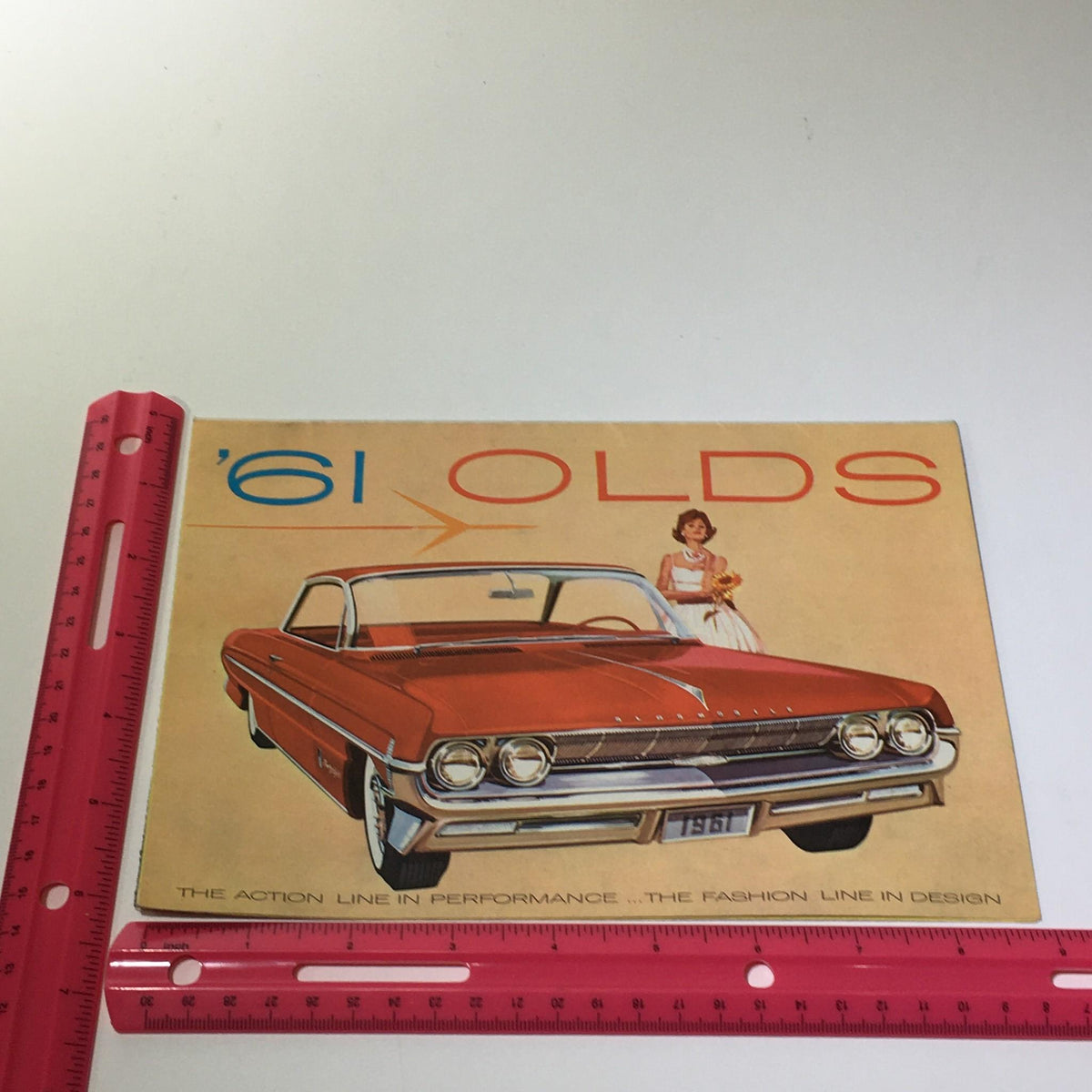 Another view of the front cover of the 1961 Oldsmobile Spirited Skyrocket Engine Hydra-Matic Drive Car Catalog Brochure with a measuring tool for size reference.