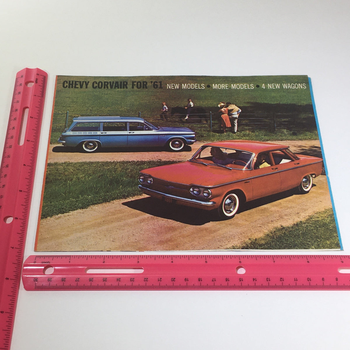 Chevy Corvair for '61 New Models-More Models-New Wagons 4-Wheel Car Catalog cover image alongside a ruler for size reference, showing two classic Corvair cars in a picturesque setting.