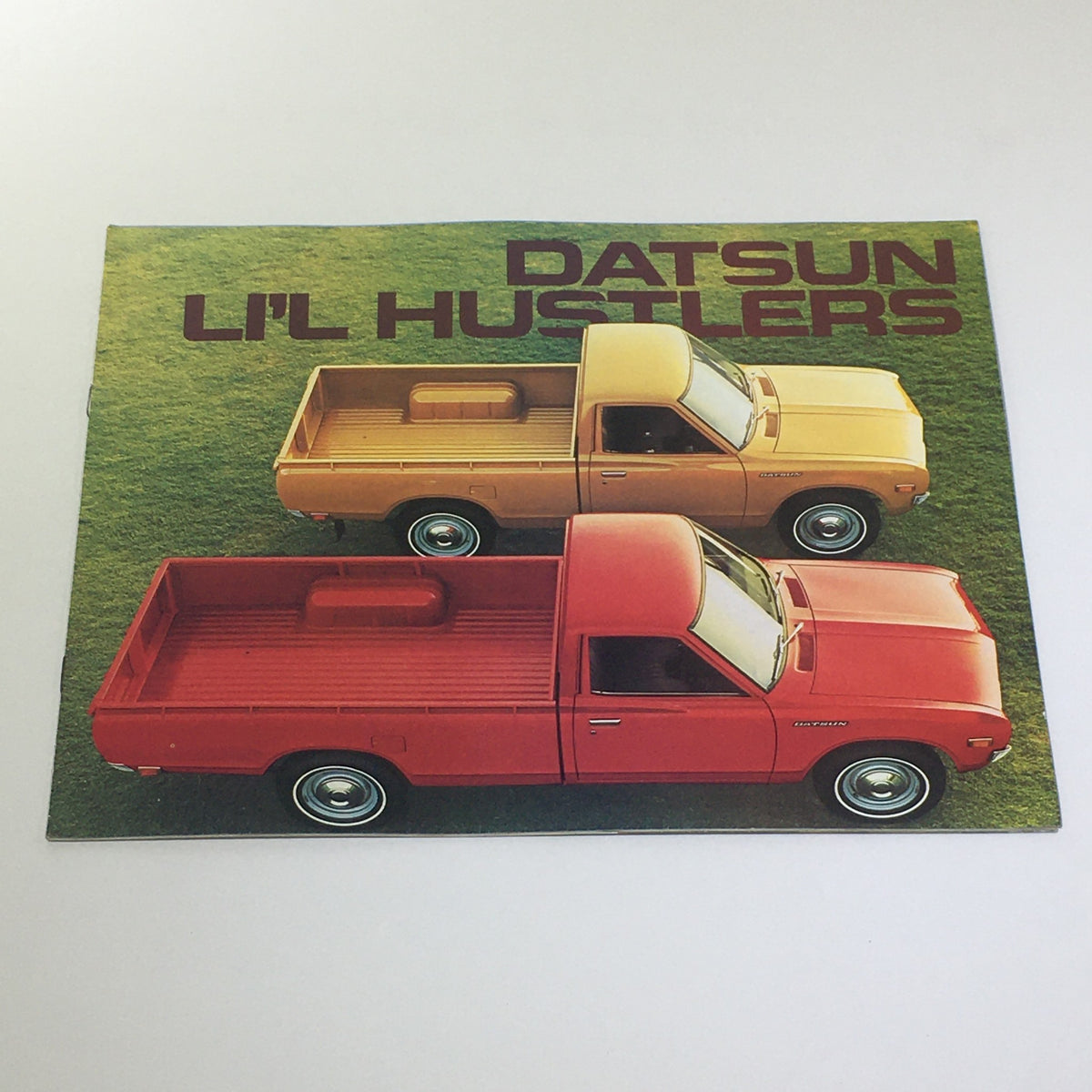 Vintage 1976 Datsun 600 Lil' Hustlers brochure featuring a colorful display of two Datsun trucks, highlighting the charming design and classic appeal of the 4-speed stick shift car.