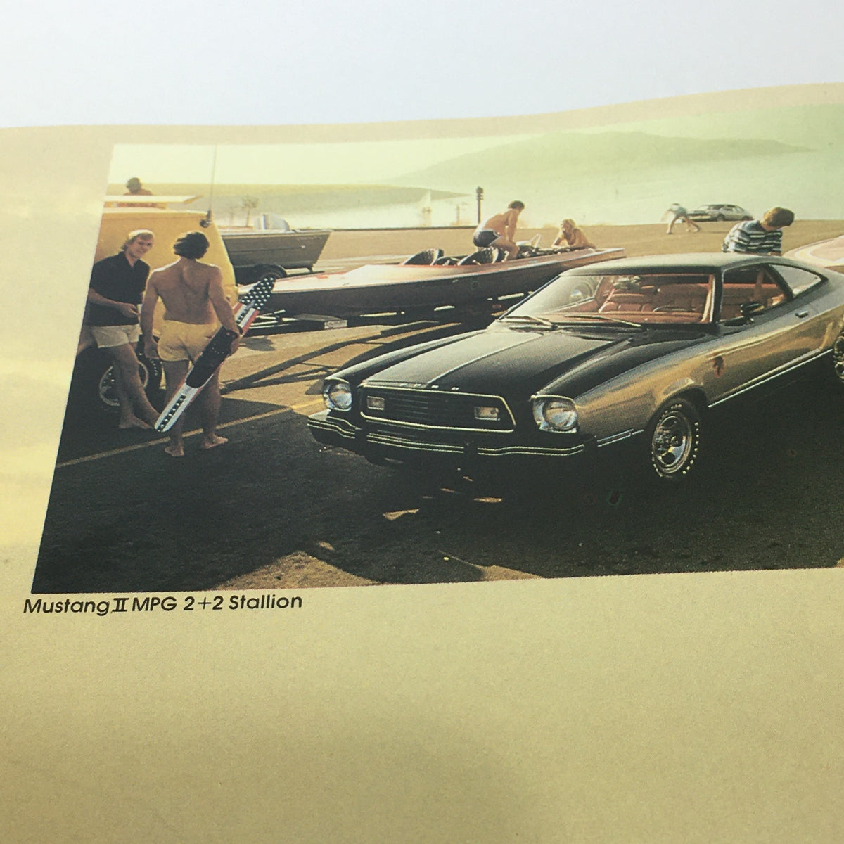 Vintage Free Wheelin' Mustang II MPG 2+2 Stallion - 1965 Shelby Cobra Car Brochure showcasing a parked Mustang II with individuals near classic boats by a scenic waterfront.