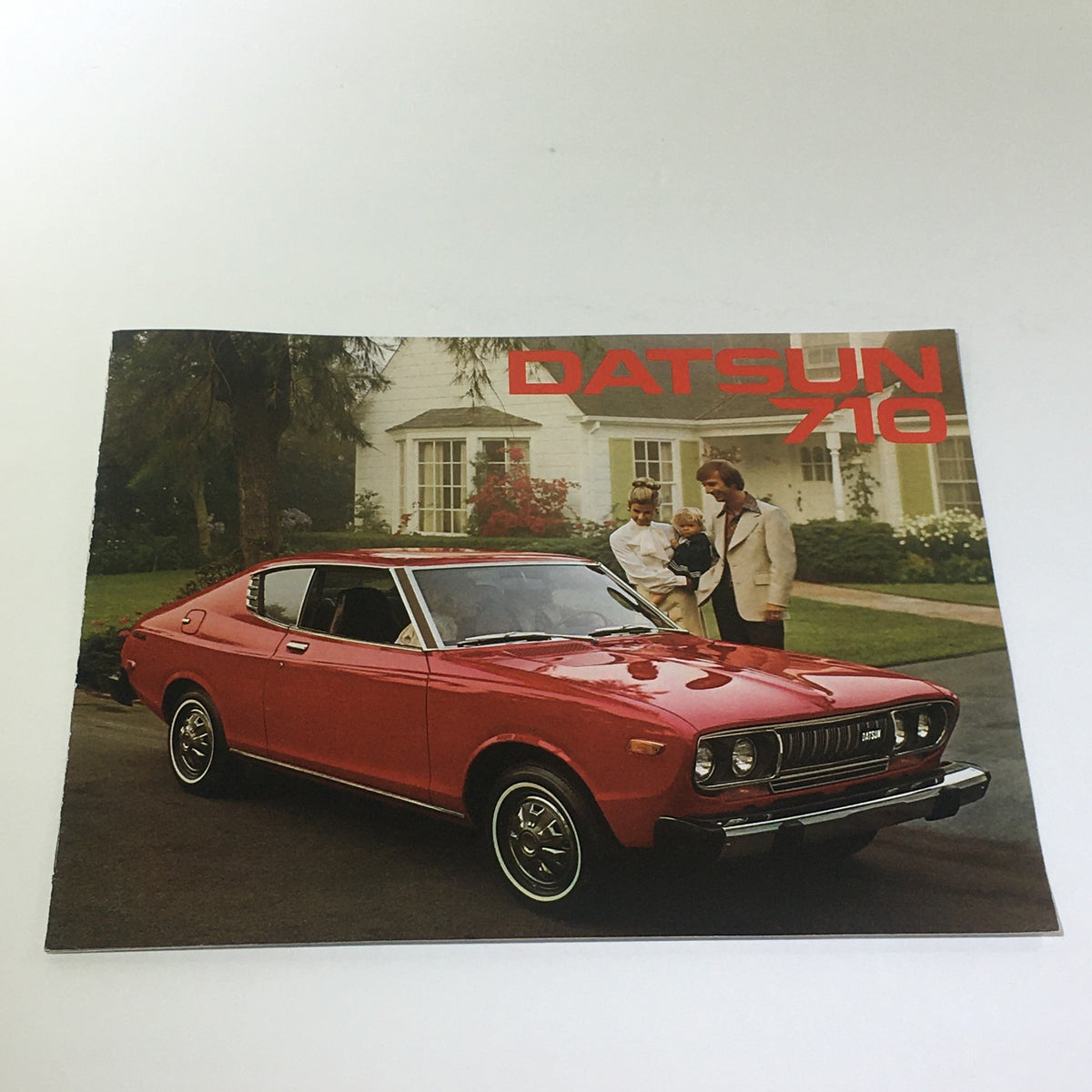 Vintage 1976 Datsun 710 2-Door Hardtop Sedan brochure featuring a red car parked outside a house with two people standing nearby.