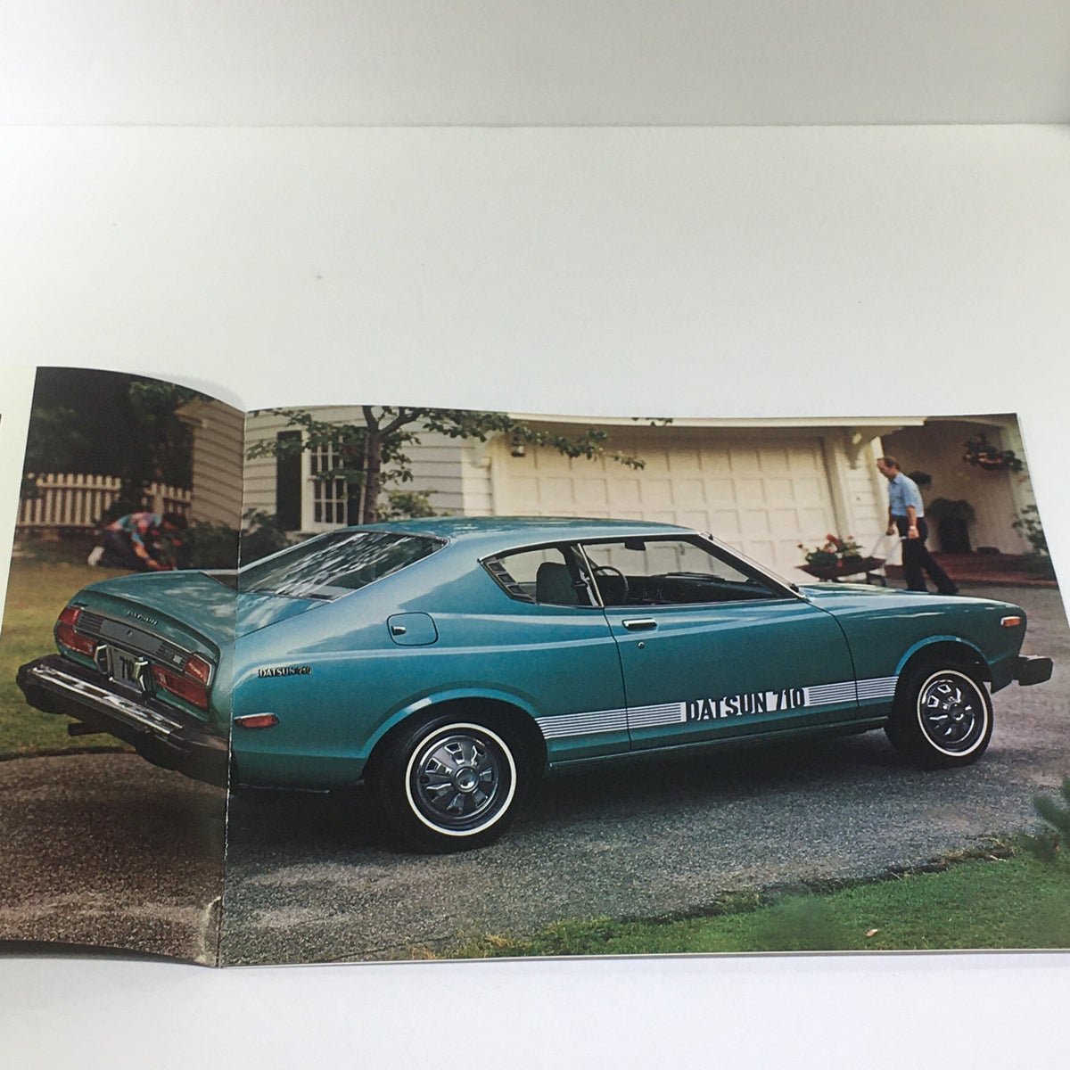 Back view of a Vintage 1976 Datsun 710 2-Door Hardtop Sedan with a teal color, parked in front of a house, showcasing its stylish design.