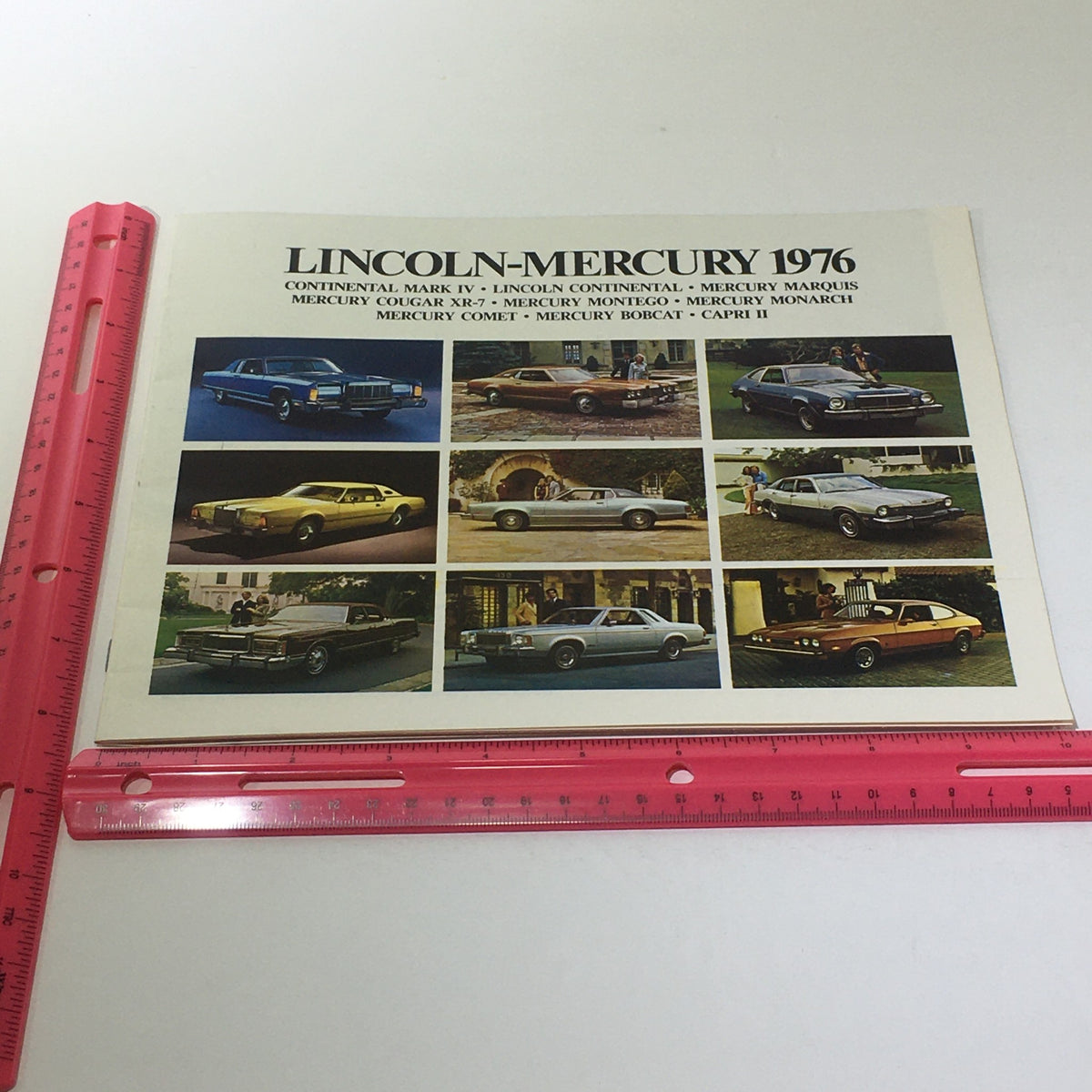 Another view of the Vintage Lincoln-Mercury 1976 Mercury Grand Monarch Ghia brochure cover with a ruler for size reference, featuring classic cars.