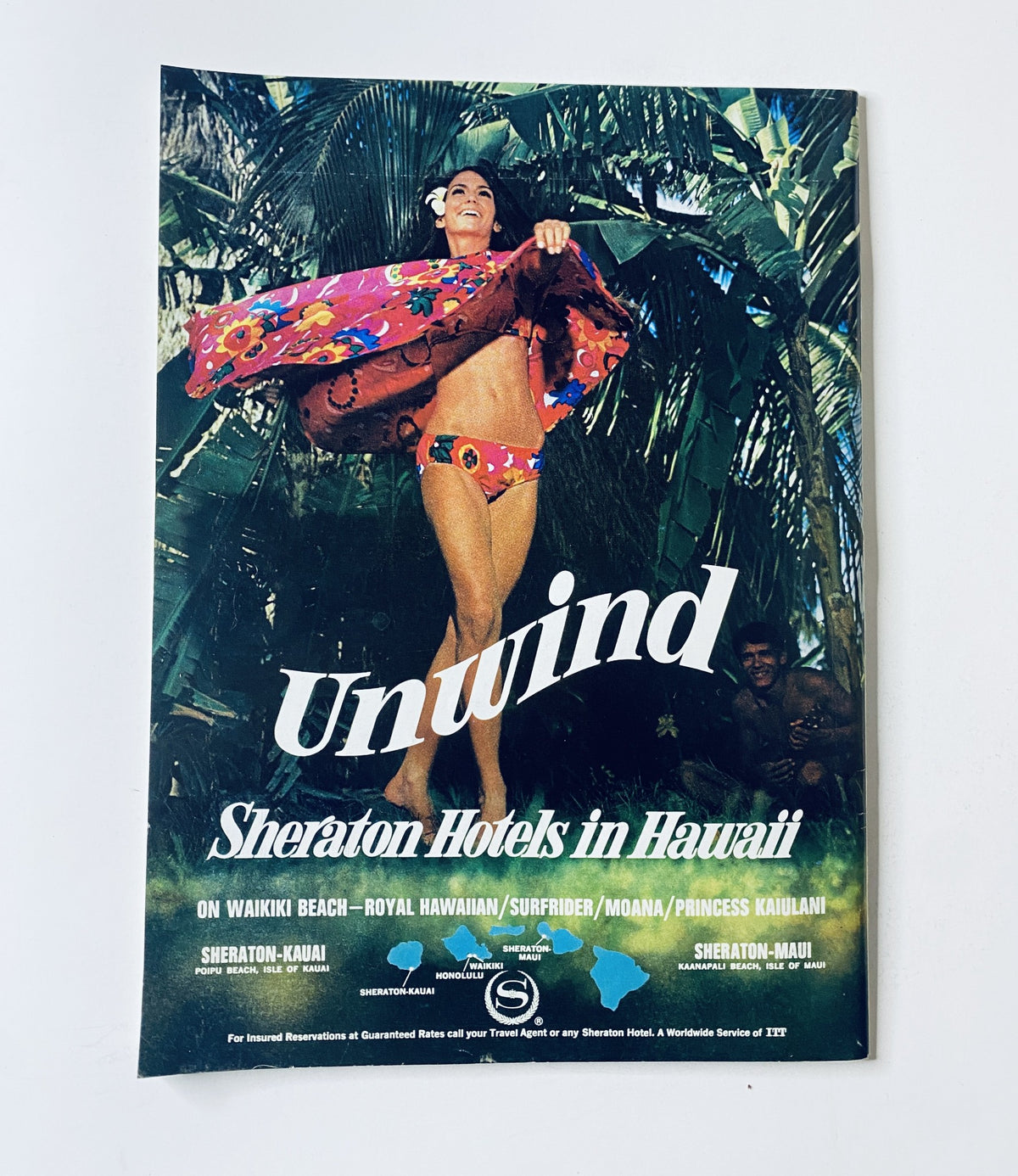 A vintage advertisement titled 'Unwind' for Sheraton Hotels in Hawaii, showcasing a woman in a colorful swimsuit and floral wrap, promoting the hotels in Waikiki Beach and Maui.