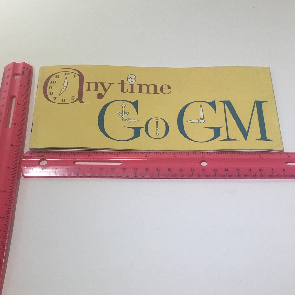 Back cover of the Vintage Go GM Any Time in the year 1963 Chevrolet-Pontiac-Buick Car Catalog, displaying a vintage design and clock motif.