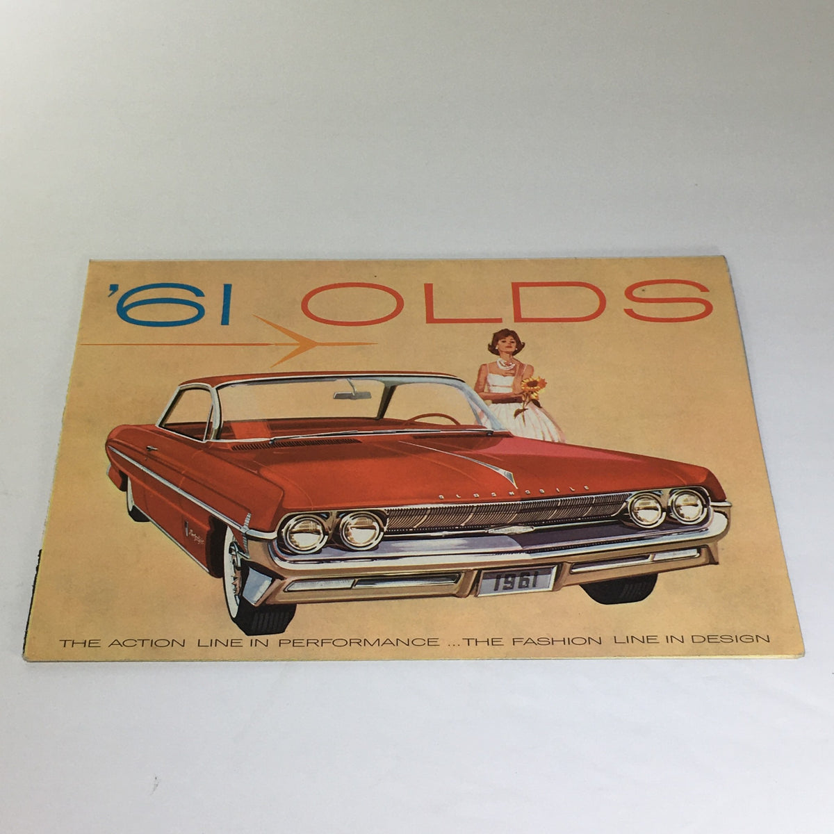 Vintage 1961 Oldsmobile 2-Door Hardtop Sedan Twin-Triangle Stability Car Catalog cover featuring a classic red car and a woman in a white dress, showcasing vintage American automotive design.