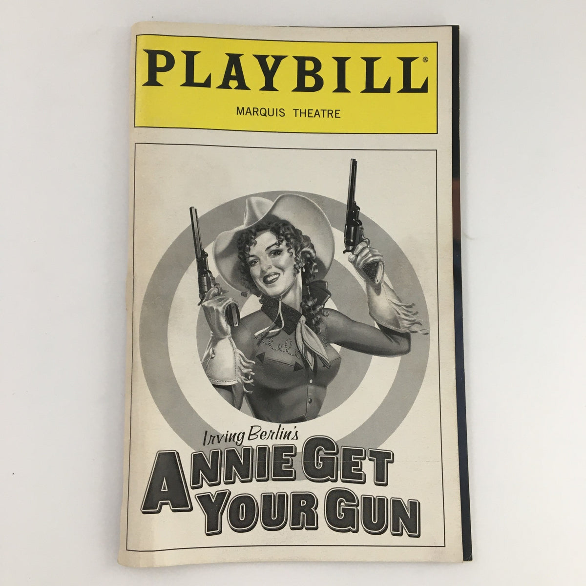 1999 Playbill for 'Annie Get Your Gun' at Marquis Theatre featuring a vintage design with a performer holding guns. Starring Tom Wopat and Valerie Wright.