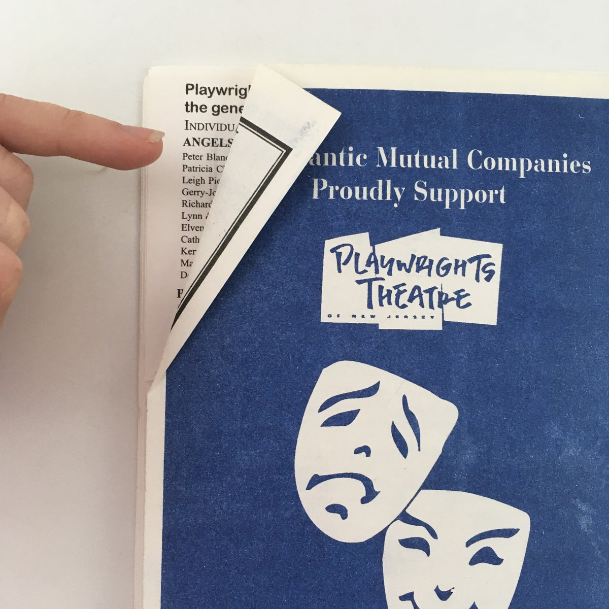 Cover detail of the 2001-2002 Playwrights Theatre ‘Visions of Peace’ by Susan Dworkin, featuring a hand pointing to the corner of the magazine with a blue background and theatrical masks.