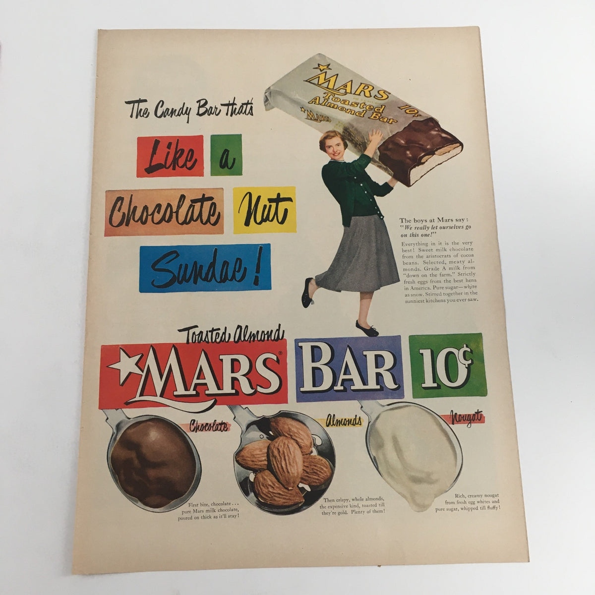 Mars Toasted Almond Bar Vintage Print Ad showcasing a woman holding a large Mars Bar and highlighting the flavors of chocolate and nuts, emphasizing its appeal as a candy bar like a chocolate nut sundae.