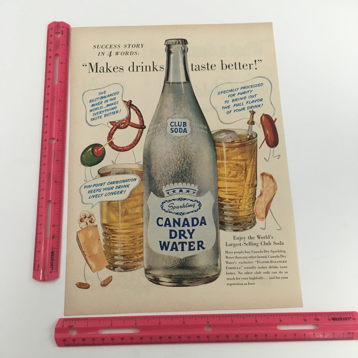 Close-up view of the vintage print ad for 1950 Club Soda Sparkling Canada Dry Water, showcasing the soda bottle and drinks with a ruler for size reference, accompanied by the tagline 'Makes drinks taste better!'.
