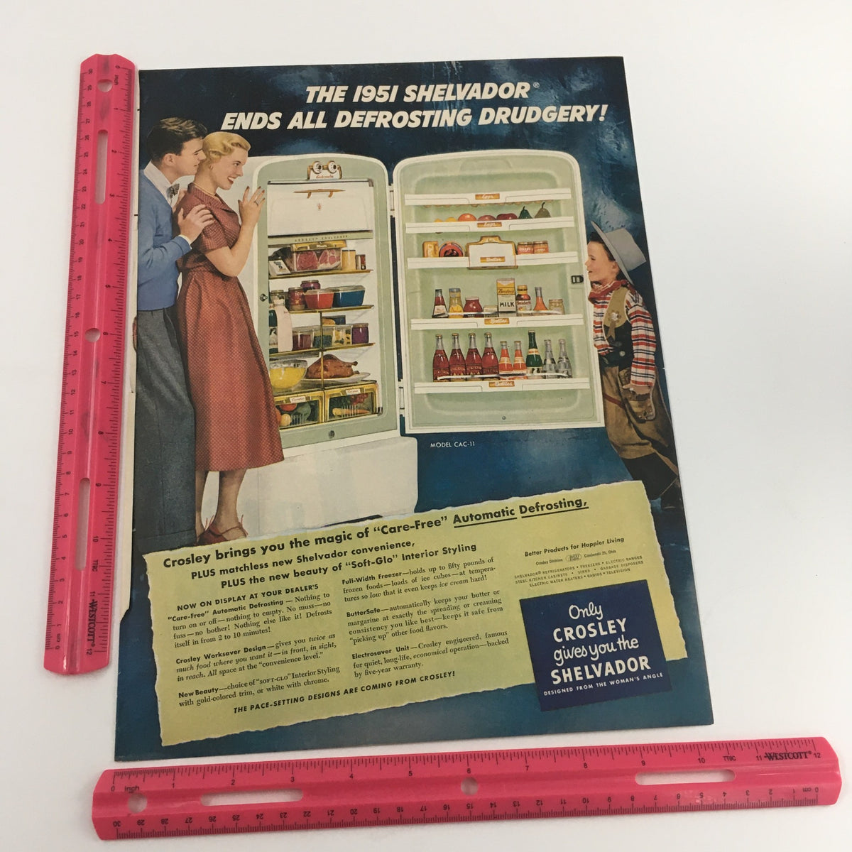 Vintage 1951 Crosley Shelvanador print ad featuring a modern kitchen, showcasing automatic defrosting technology. The ad displays a refrigerator filled with food items, with a family enjoying the convenience, encapsulating mid-century American home life.