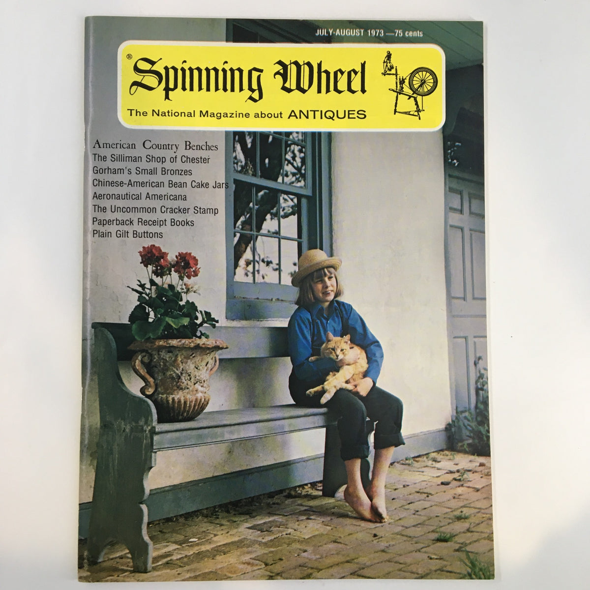 Cover of Spinning Wheel Magazine July-August 1973 featuring the theme 'American County Benches'. The cover displays a child with a cat sitting on a country bench, framed by a window with flowers.