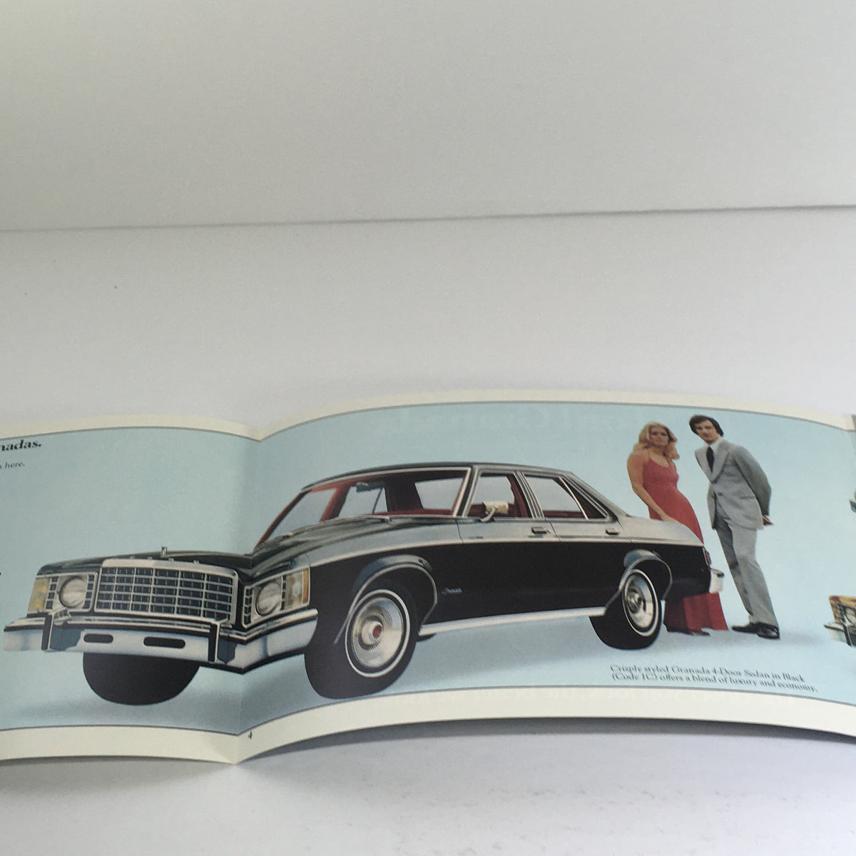 1975 Ford Granada Ghia Option Highlights car dealership promotional image featuring the vehicle with a couple in elegant attire, showcasing the car's design.