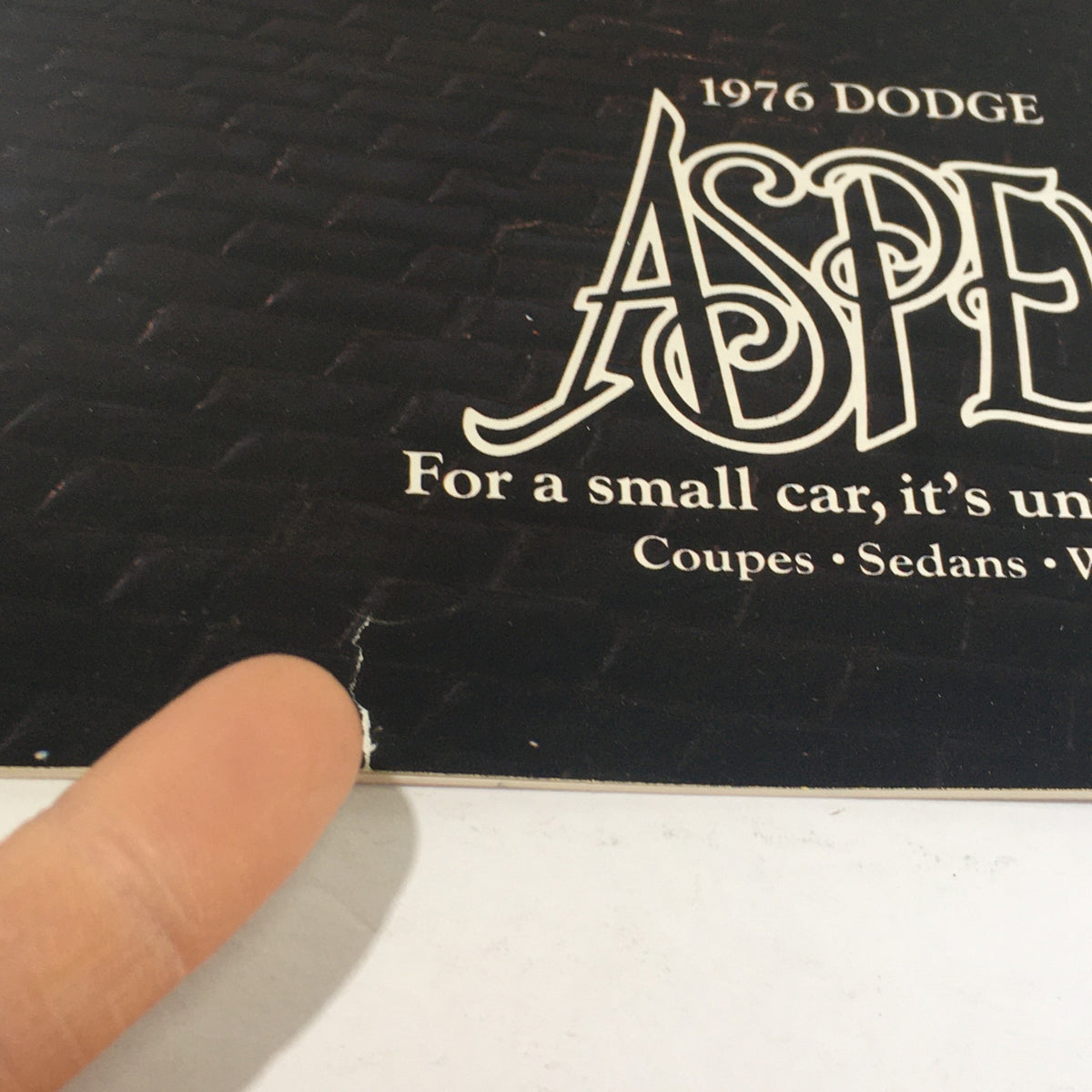 Close-up of the 1976 Dodge Aspen logo on a brochure, highlighting minor damage and wear. Dealership car auto brochure catalog.