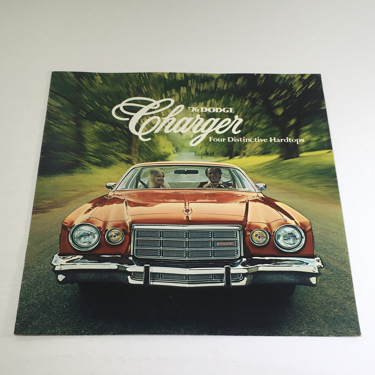 Cover of the 1976 Dodge Charger brochure featuring a vintage orange Charger with two people inside, showcasing the car's iconic design and classic style.