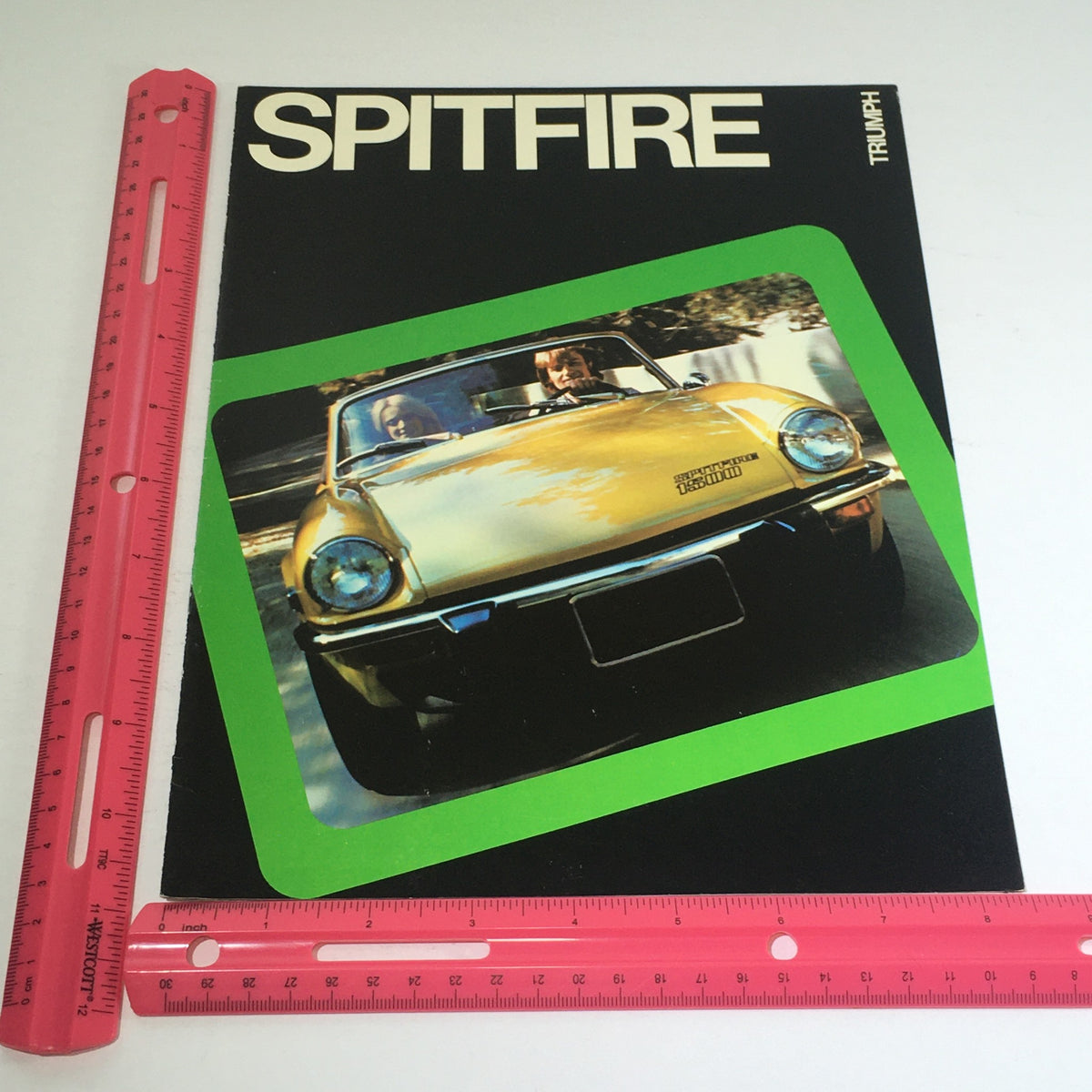 Close-up of the 1975 Spitfire Triumph Dealership Specification Car Auto Brochure Catalog cover with a ruler for scale, highlighting its vintage appeal.