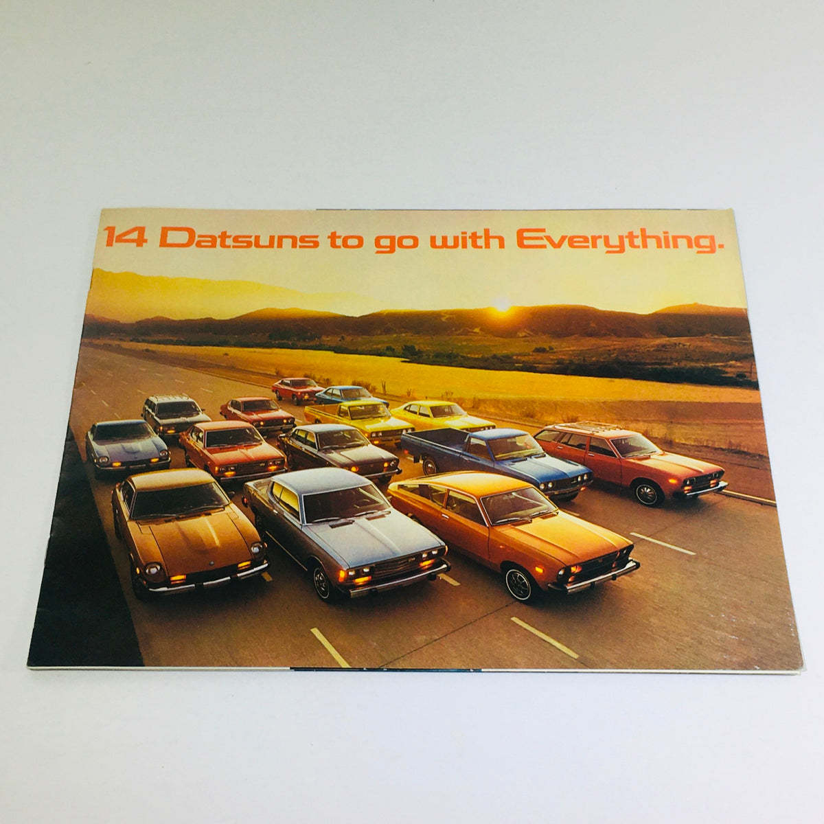 1976 Datsun 280-Z/MSA GTU Dealership Car Auto Brochure Catalog cover featuring a vibrant sunset and multiple Datsun cars on the road showcasing the brand's diverse lineup.