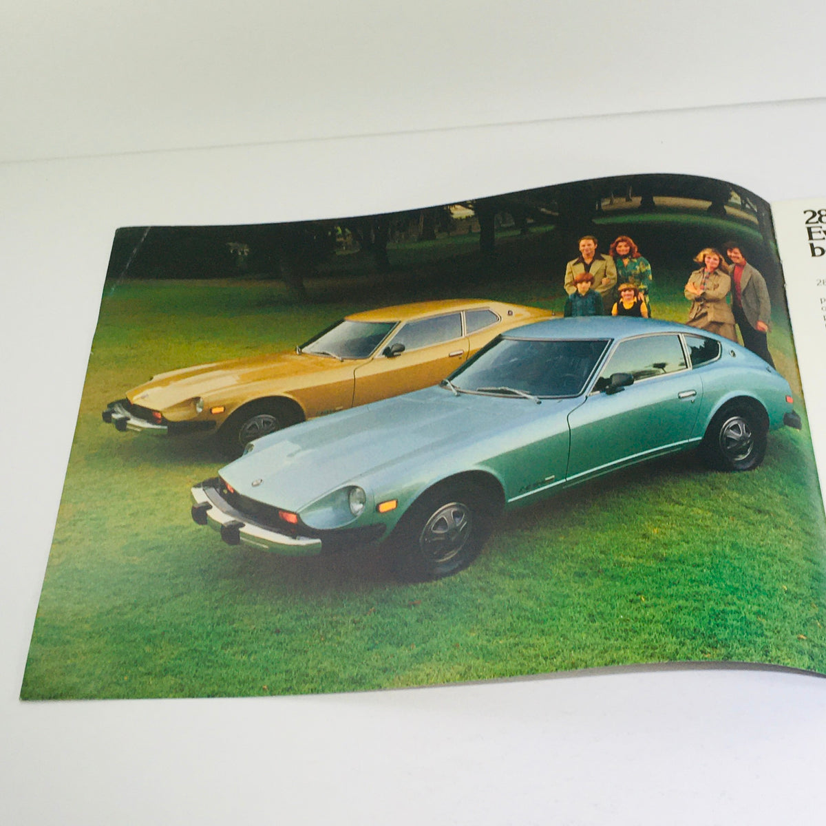 1976 Datsun 280-Z/MSA GTU Dealership Car Auto Brochure Catalog image displaying a yellow and a teal Datsun car parked on grass with a group of people posing nearby.