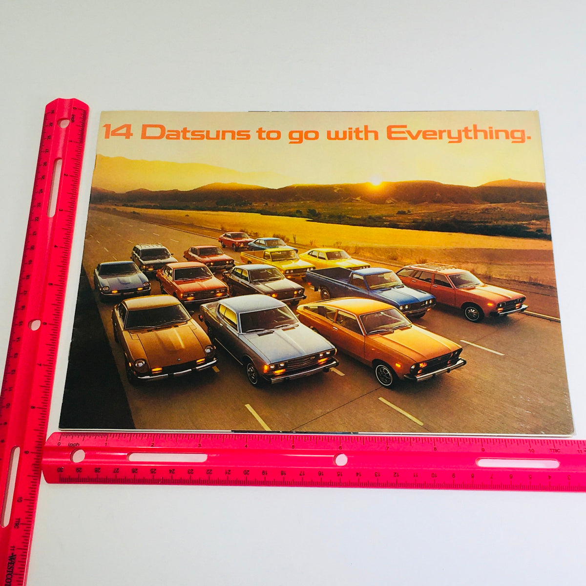 1976 Datsun 280-Z/MSA GTU Dealership Car Auto Brochure Catalog showcasing a vibrant collection of Datsun cars on a picturesque road at sunset, highlighting 14 models with the tagline '14 Datsuns to go with Everything.'