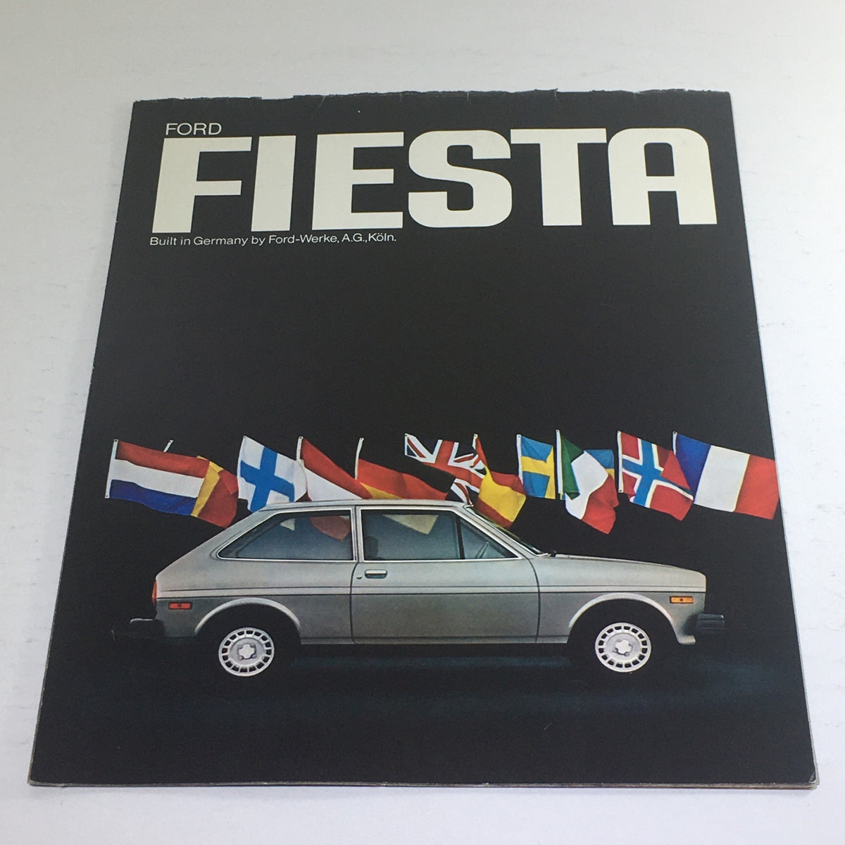 Cover image of the 1976 Ford Fiesta 3-Door Hatchback Dealership Car Auto Brochure Catalog, featuring the classic car with flags from various countries in the background.