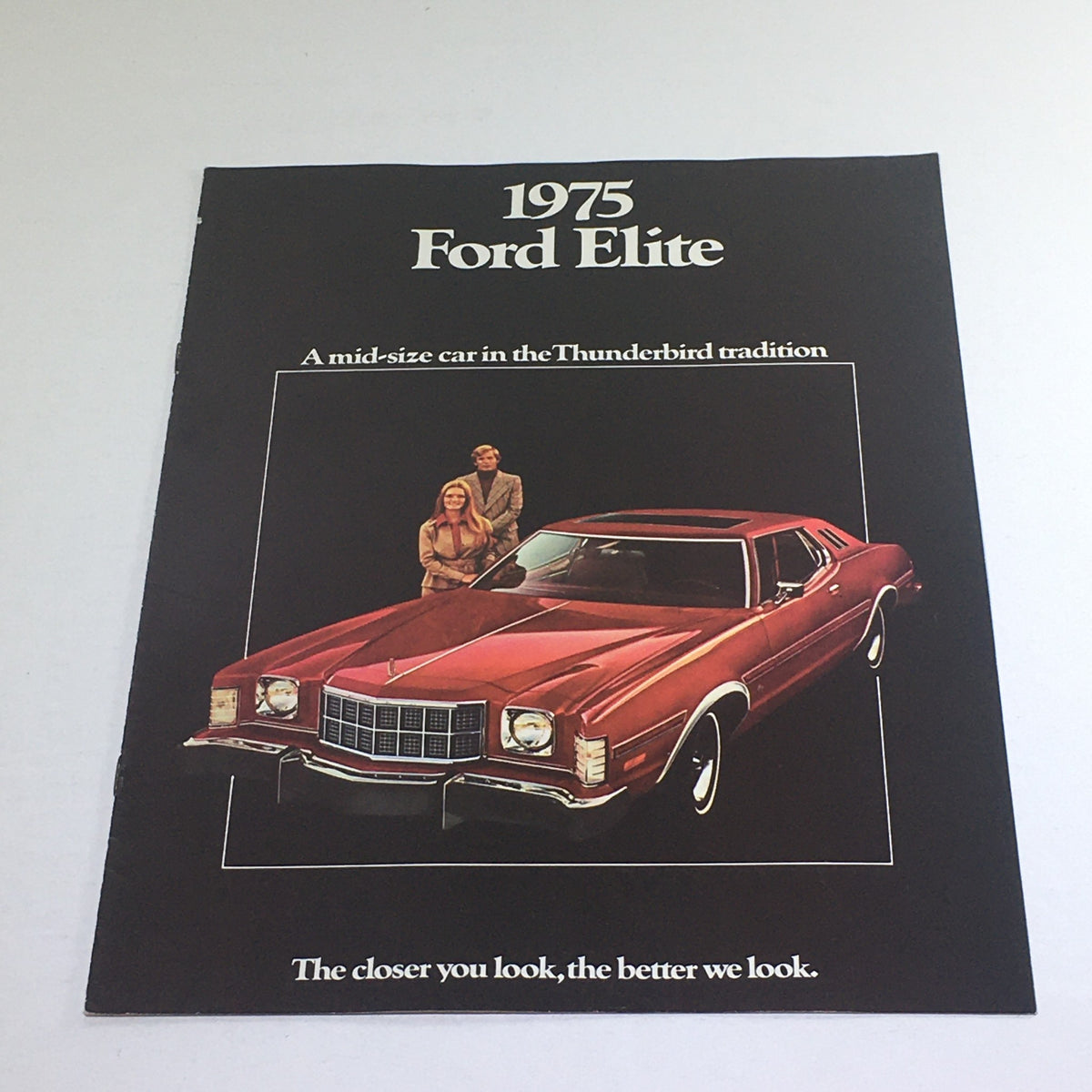1975 Ford Elite Thunderbird Edition dealership brochure cover featuring a red car and a couple standing beside it, stating 'A mid-size car in the Thunderbird tradition.'
