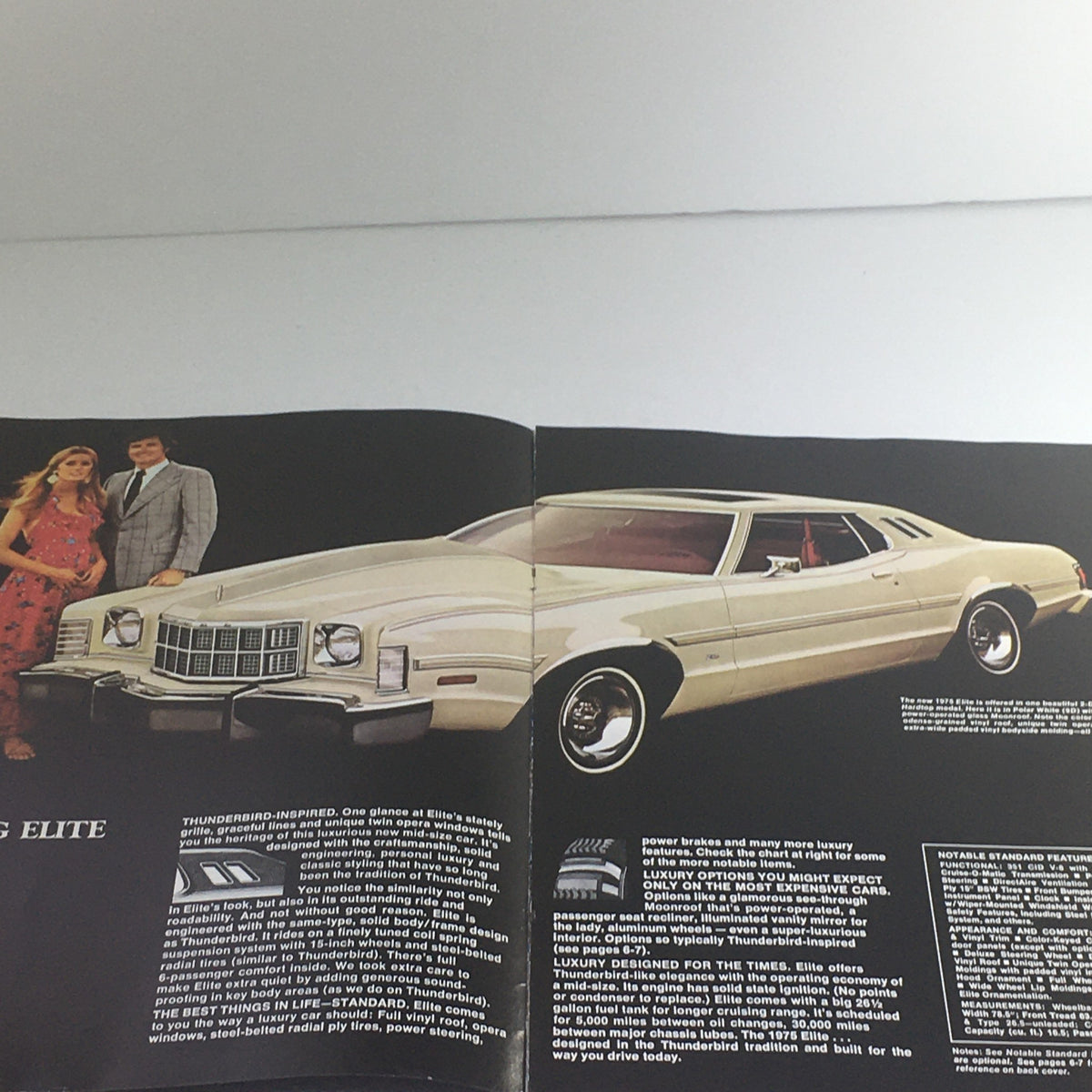 Interior view of the 1975 Ford Elite Thunderbird Edition brochure showcasing a white Ford Elite car with a couple, with detailed text about the car's features.