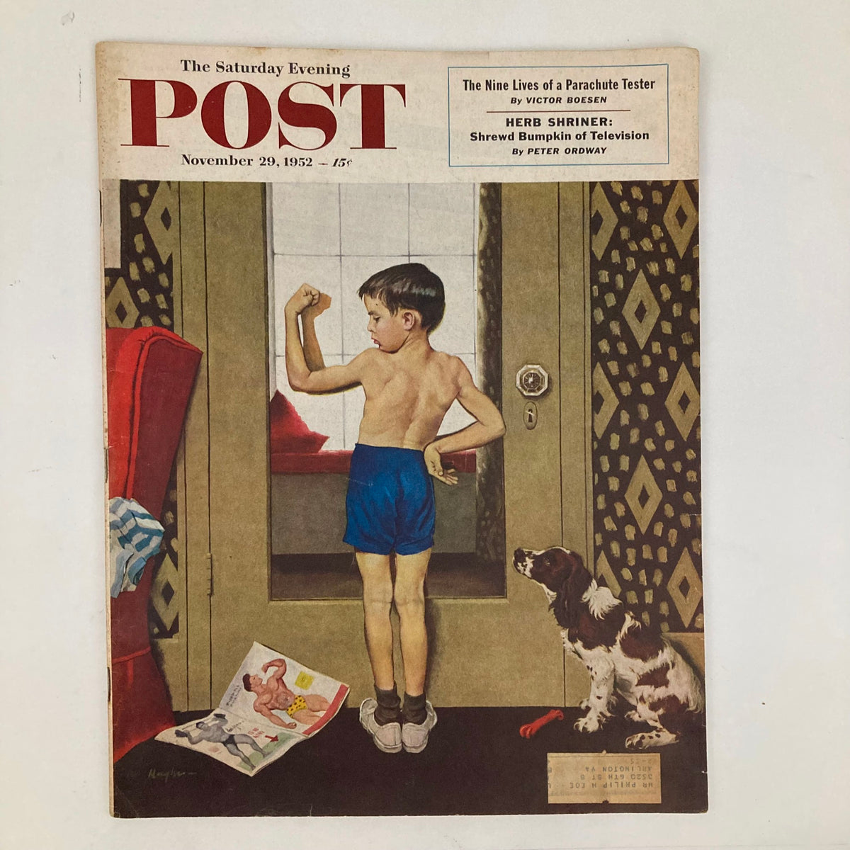 Cover of Saturday Evening Post Magazine from November 29, 1952, featuring a young boy flexing his muscles in blue shorts, standing in front of a doorway with a dog nearby and magazines scattered on the floor, illustrated by George Hughes.