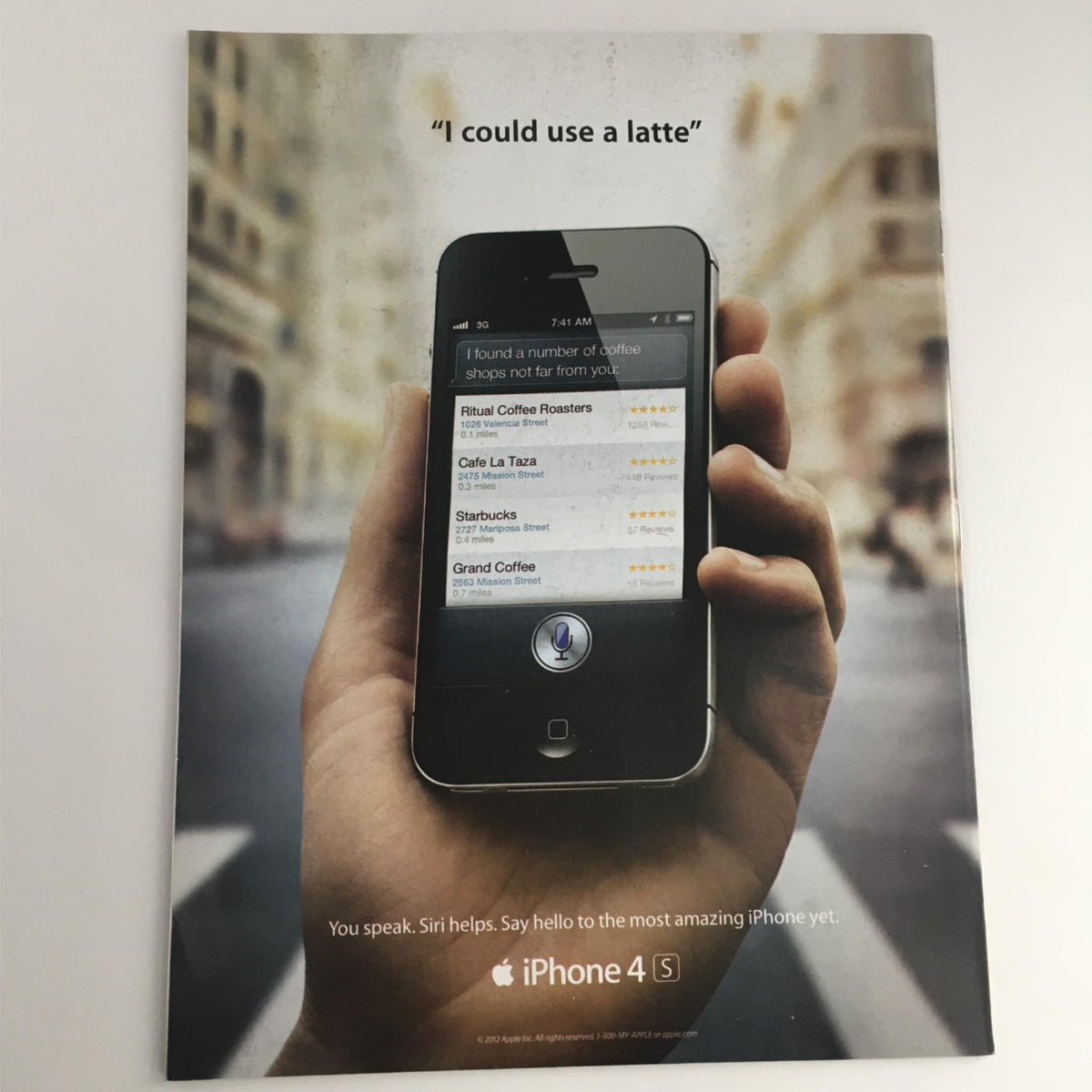 Advertisement for iPhone 4S showcasing Siri capability with a hand holding the device, featuring the phrase 'I could use a latte'.