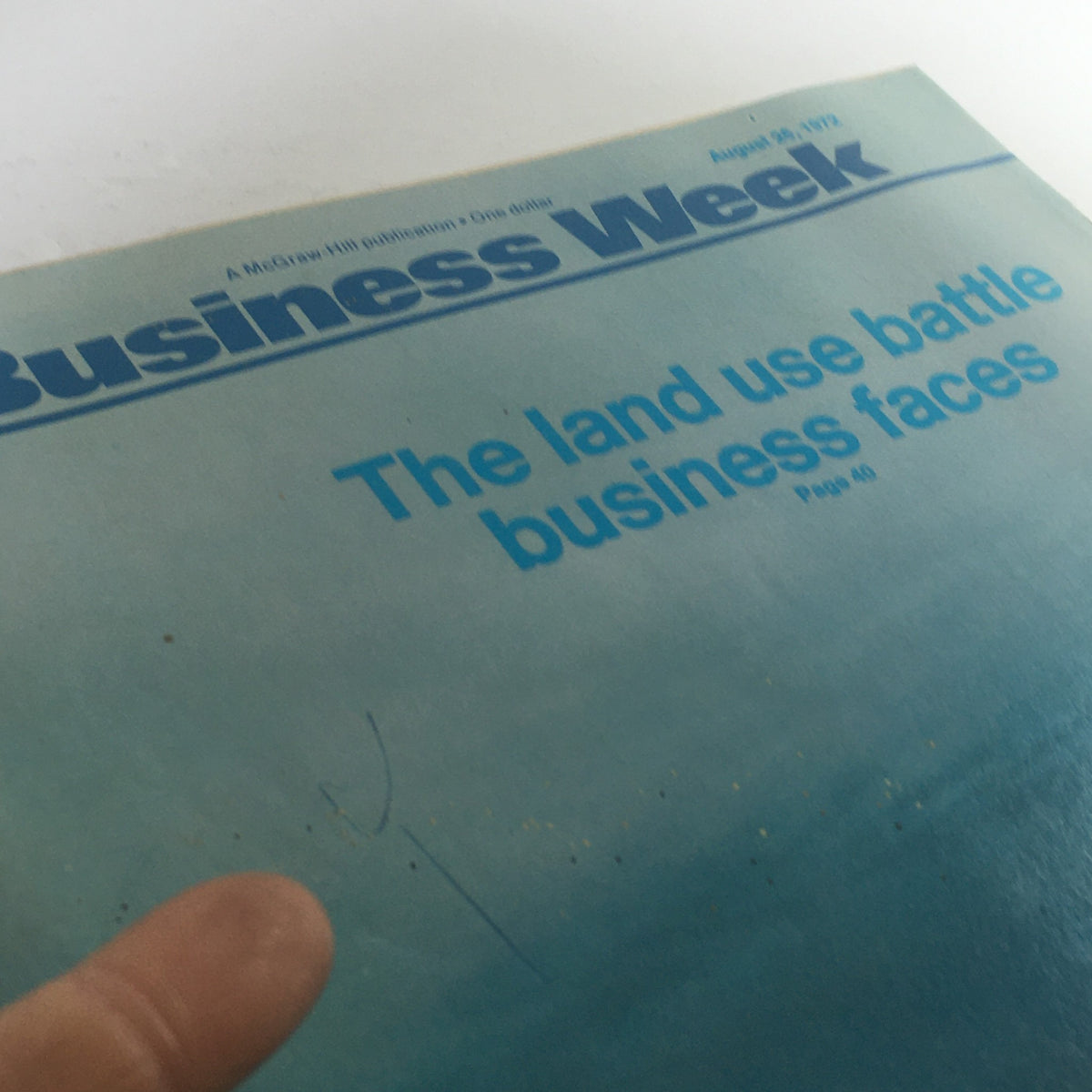 Close-up view of the Business Week Magazine cover from August 26, 1972, emphasizing the title 'The Land Use Battle Business Faces.' The image shows a finger pointing at the title on the cover, with signs of wear visible.