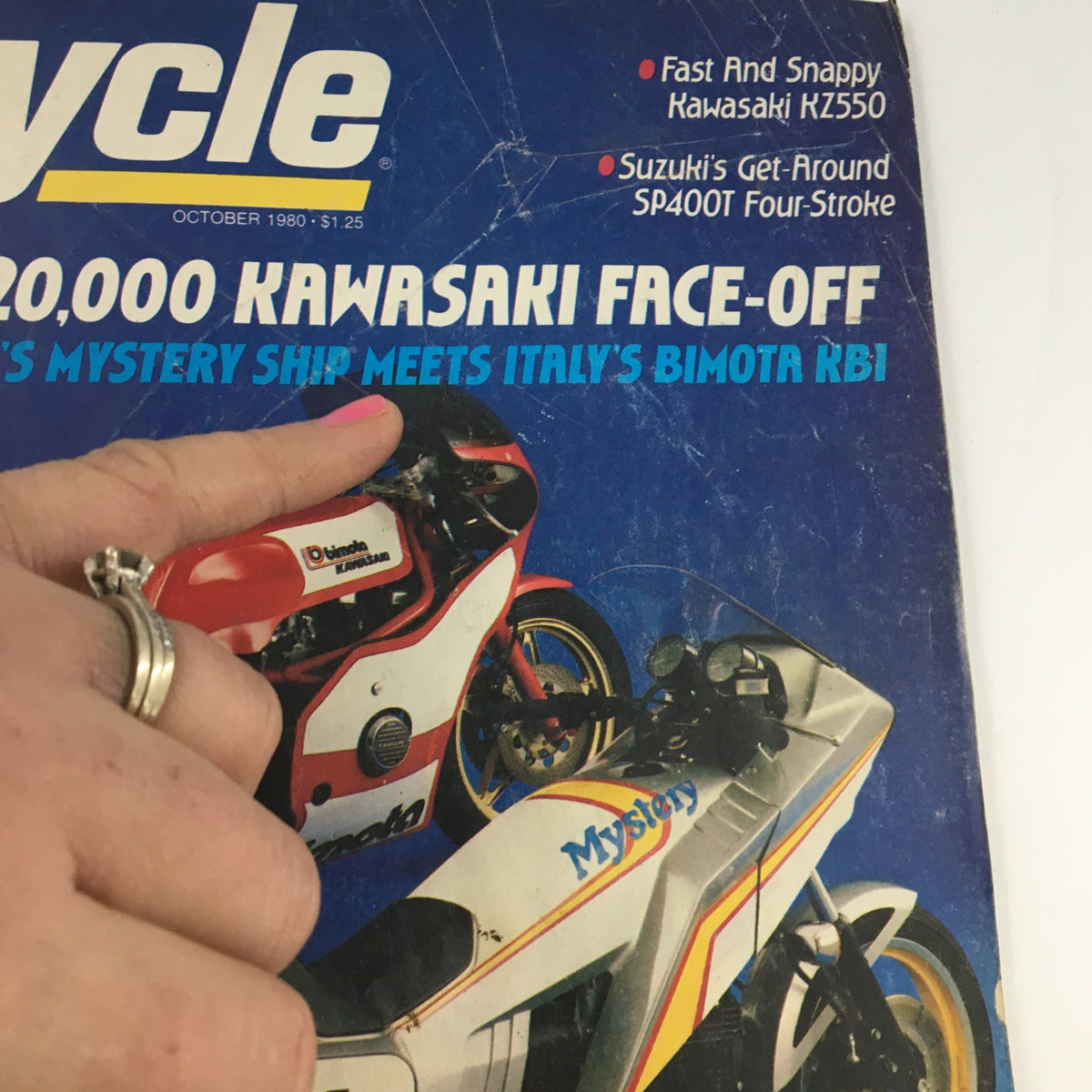 Close-up view of Cycle Magazine October 1980 cover showcasing Bimota KB1 and Kawasaki KZ550 with a finger pointing at the magazine details, reflecting classic motorcycle culture.